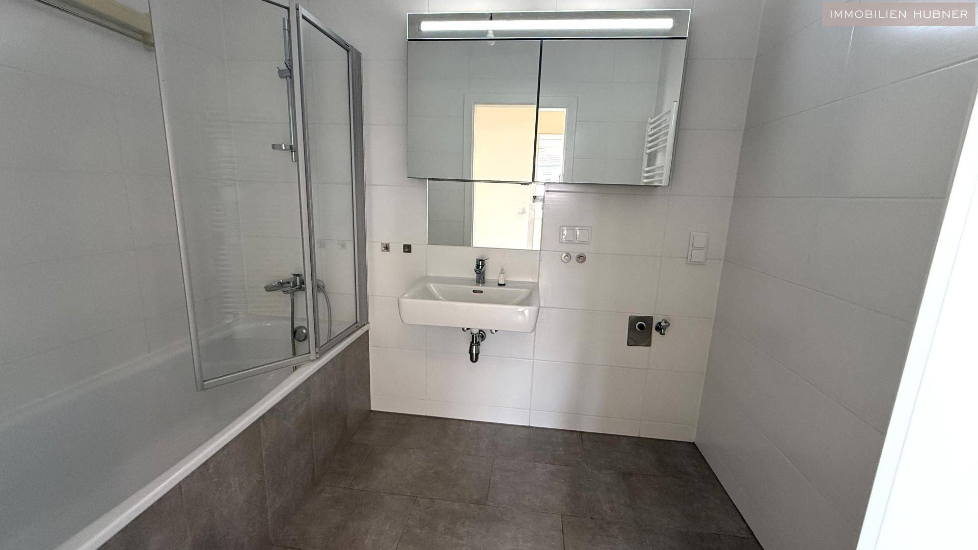 Modernes Badezimmer mit Badewanne, Duschabtrennung, Einzelwaschbecken und Spiegelschrank.