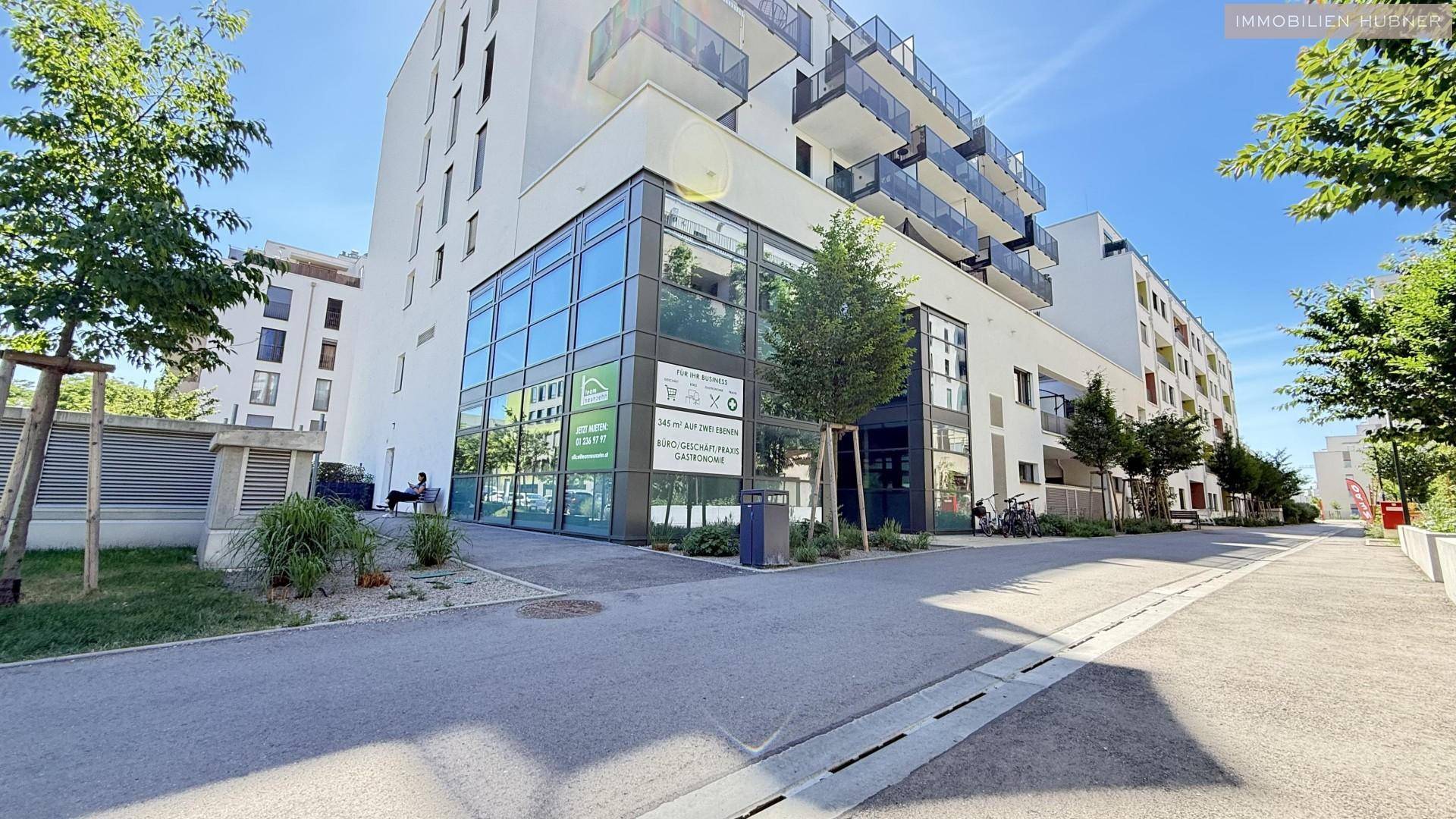 Modernes Wohn- und Geschäftsgebäude mit Glasfassade und Balkonen unter strahlend blauem Himmel.