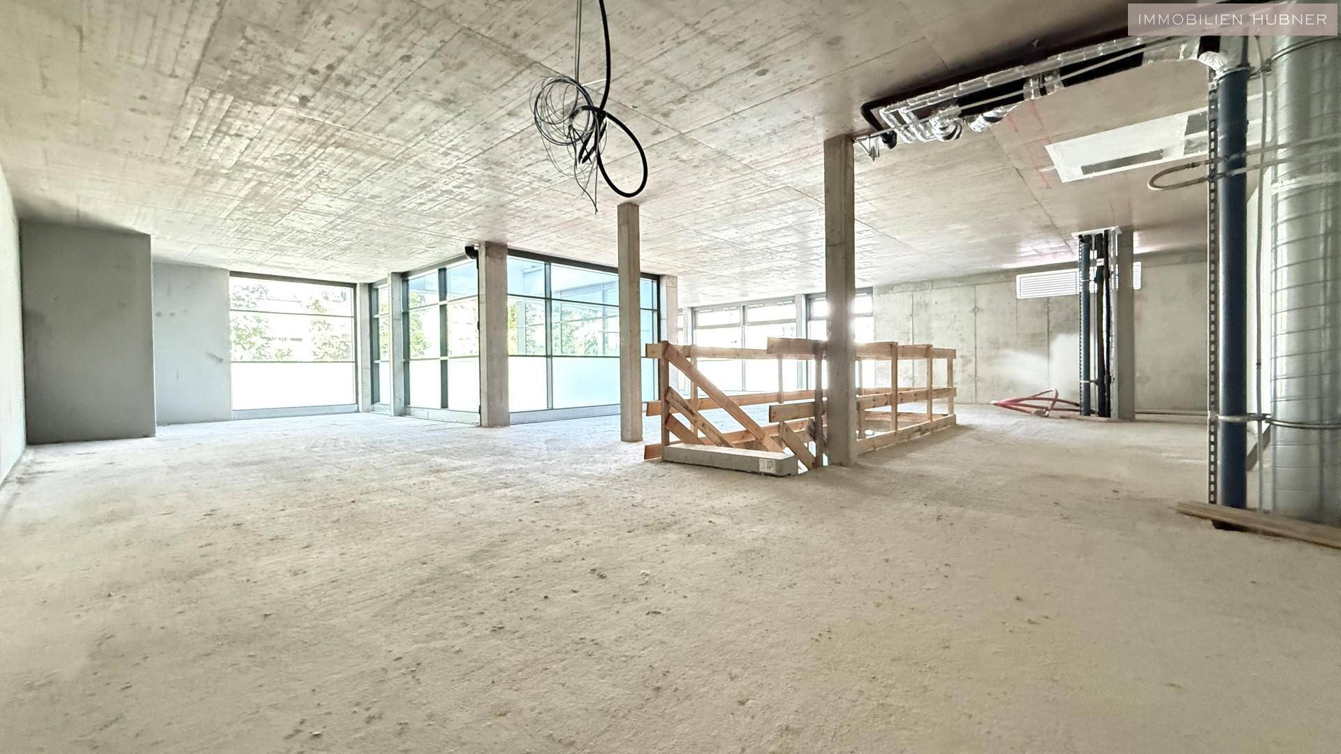 Weitläufiger Rohbau-Gewerberaum mit sichtbaren Deckeninstallationen und viel Tageslicht.
