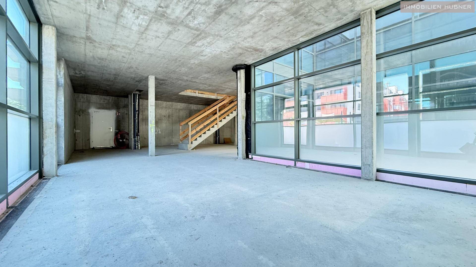 Heller Gewerberaum im Rohbau mit Betonstützen und breiten Fensterflächen, die viel Licht hereinlassen.