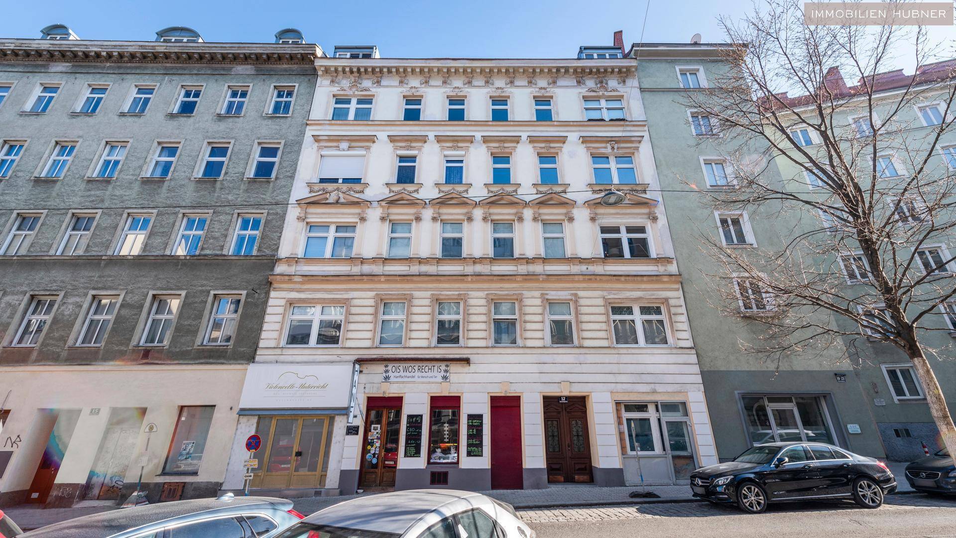 Klassische Fassade eines Mehrfamilienhauses an einer städtischen Straße mit Geschäften im Erdgeschoss.