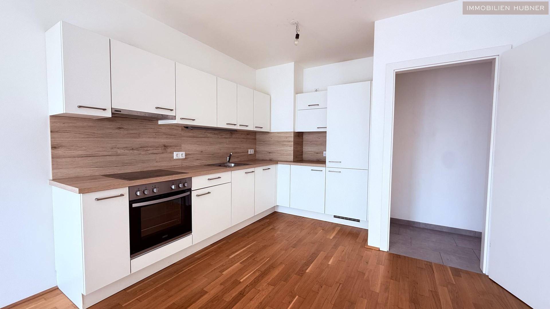 Moderne Einbauküche mit weißen Schränken, Holzarbeitsplatte und Parkettboden in hellem Design.