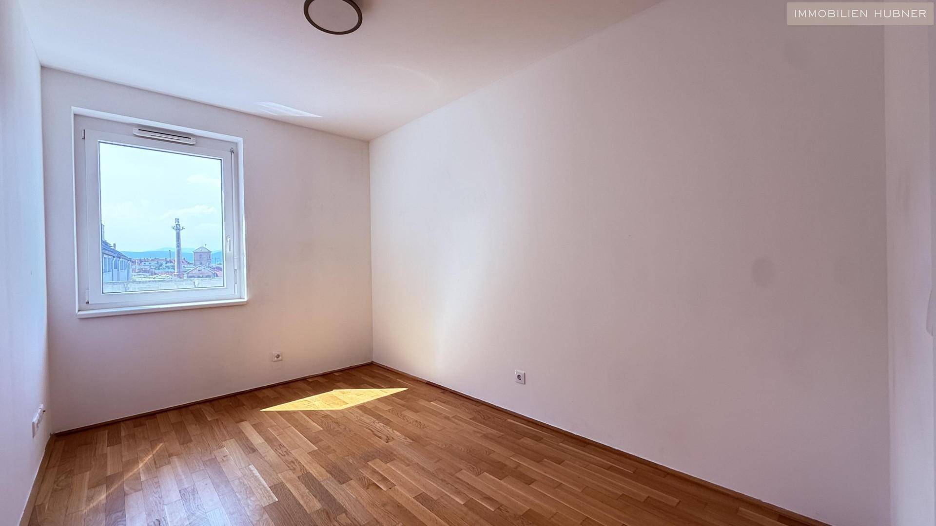 Helles Schlafzimmer mit Parkettboden und einem Fenster, das eine weite Aussicht bietet.