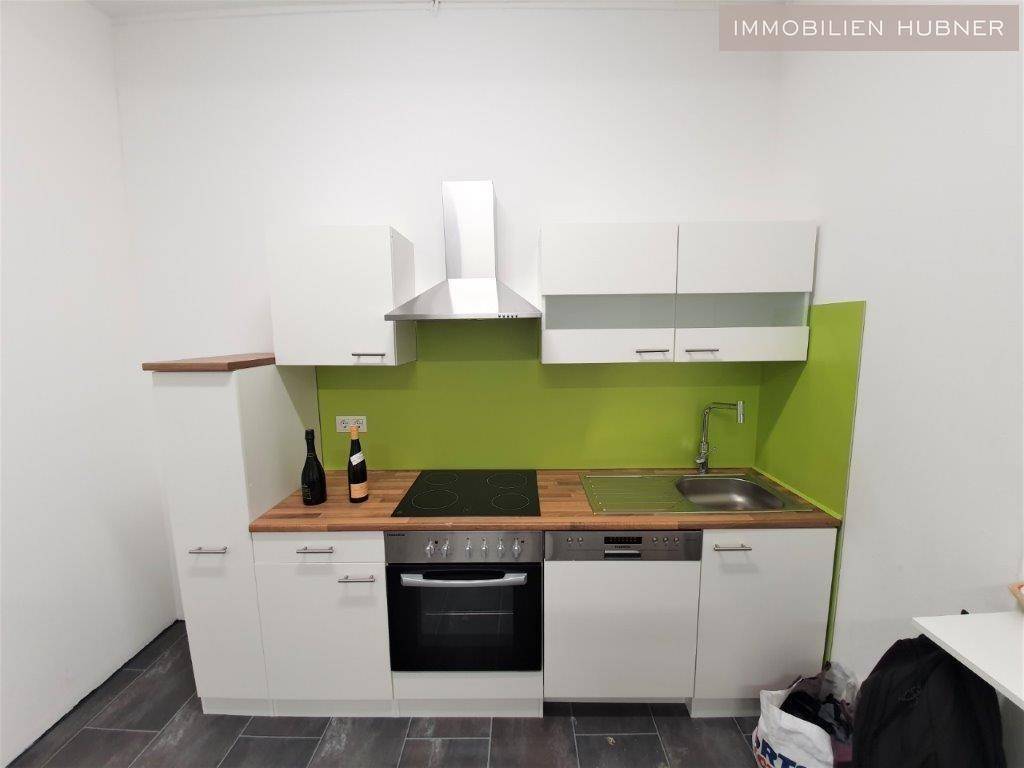 Kleine Einbauküche mit Holztheke, Spüle, Kochfeld und einem auffälligen grünen Fliesenspiegel.
