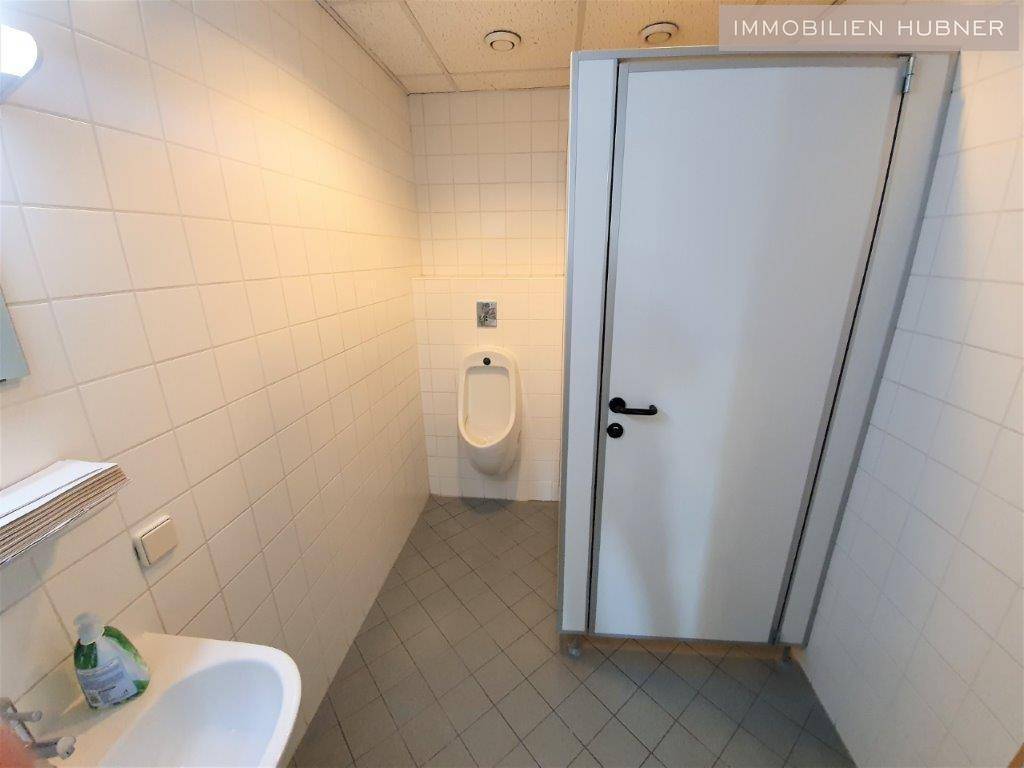 Funktionaler Sanitärraum mit weißen Fliesen, einem Urinal und einem kleinen Waschbecken.