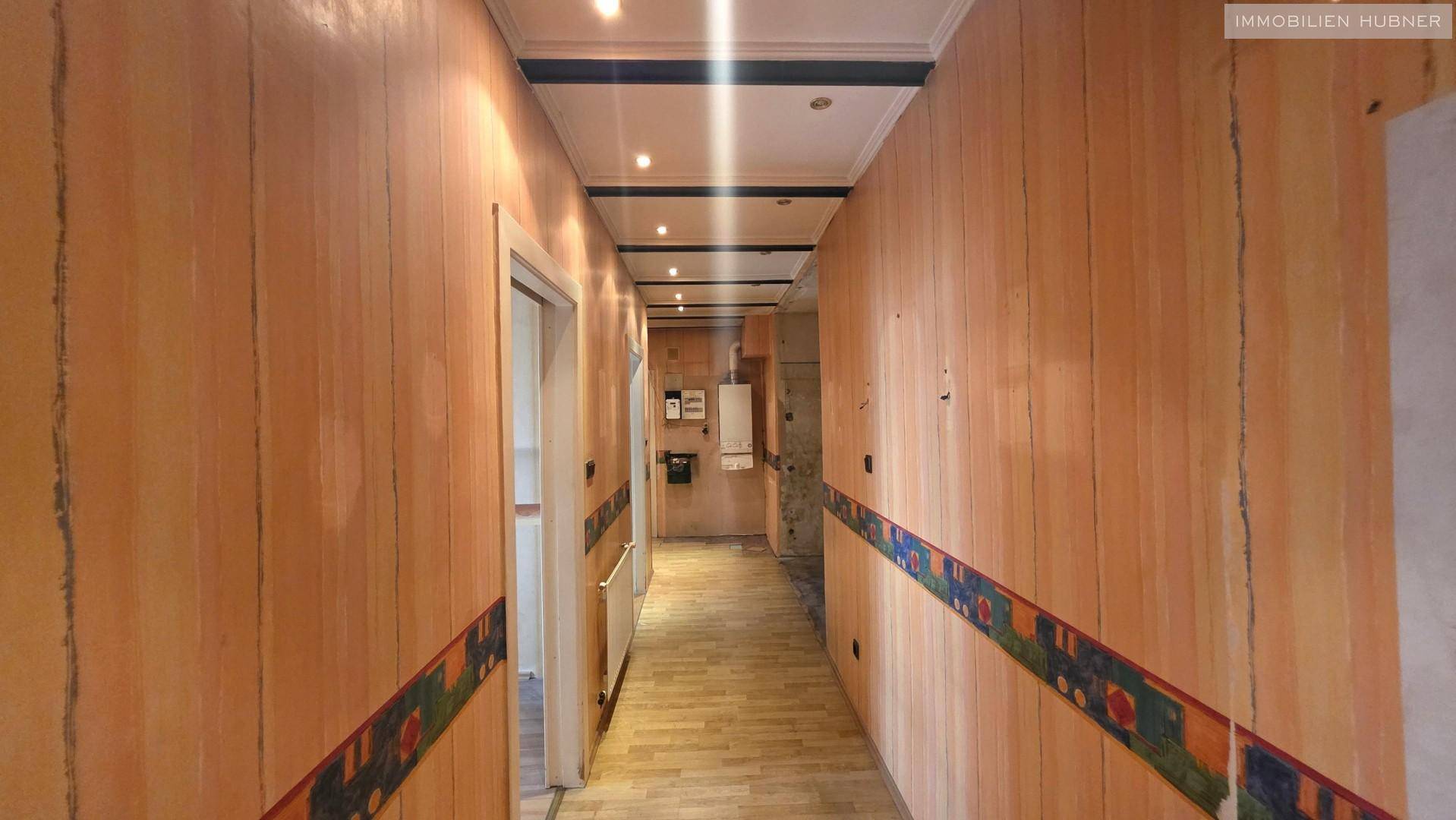 Langer Flur mit Holzverkleidung und Laminatboden, führt zu weiteren Räumen der Wohnung.
