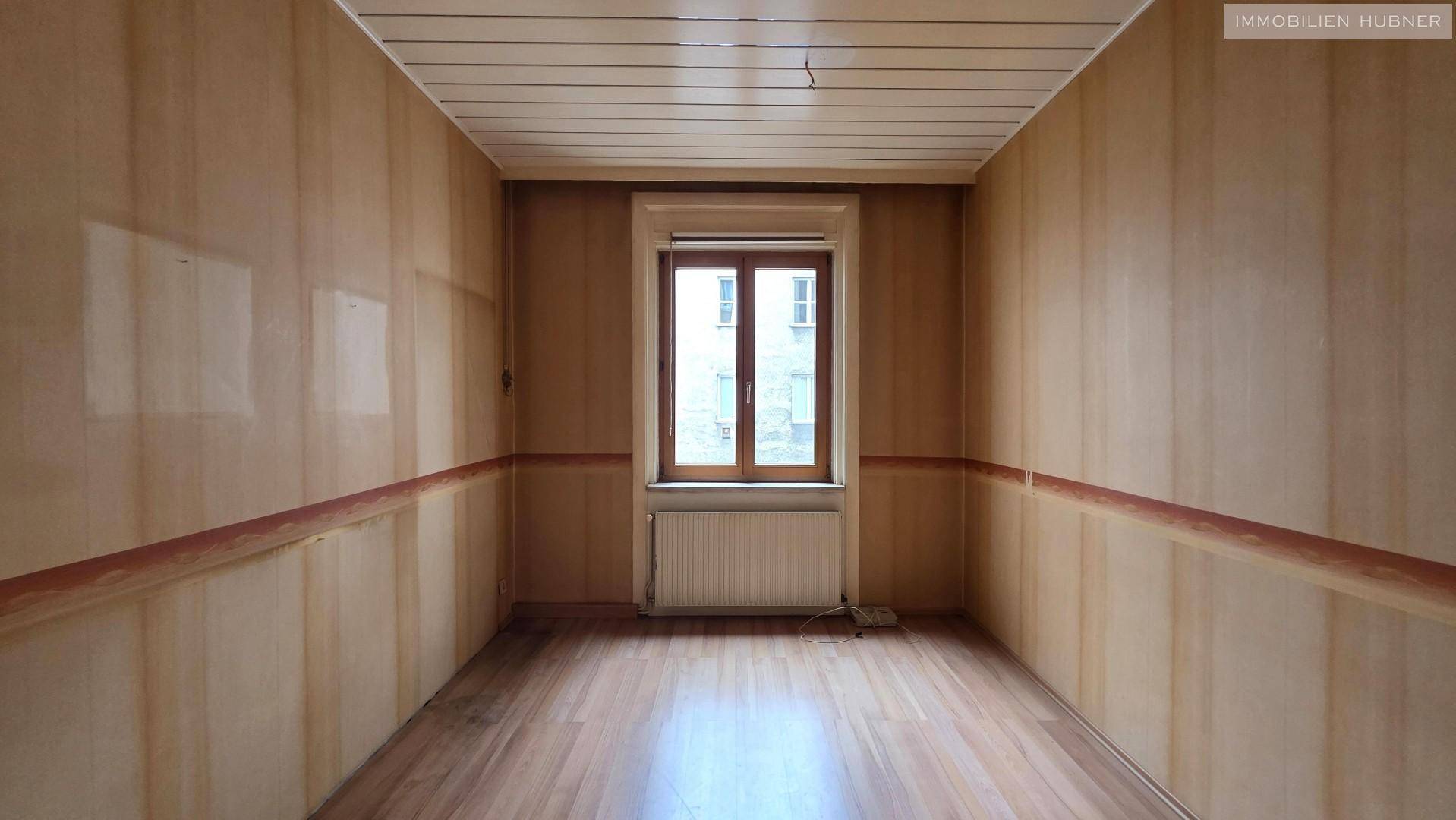 Leeres Zimmer mit Holzverkleidung und Laminatboden, bereit für individuelle Gestaltung und Nutzung.