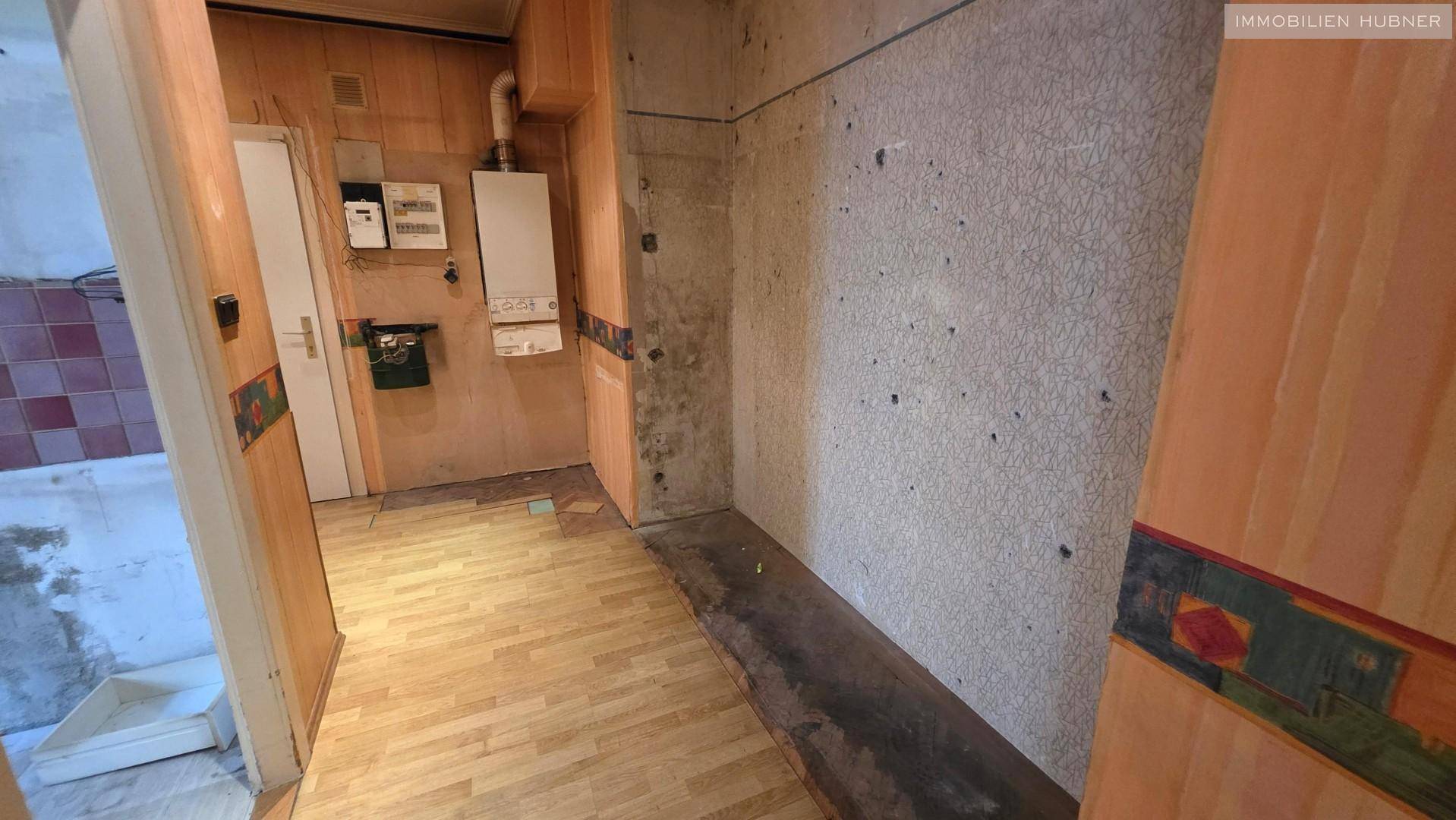 Flurbereich mit Gastherme und Laminatboden, in renovierungsbedürftigem Zustand.