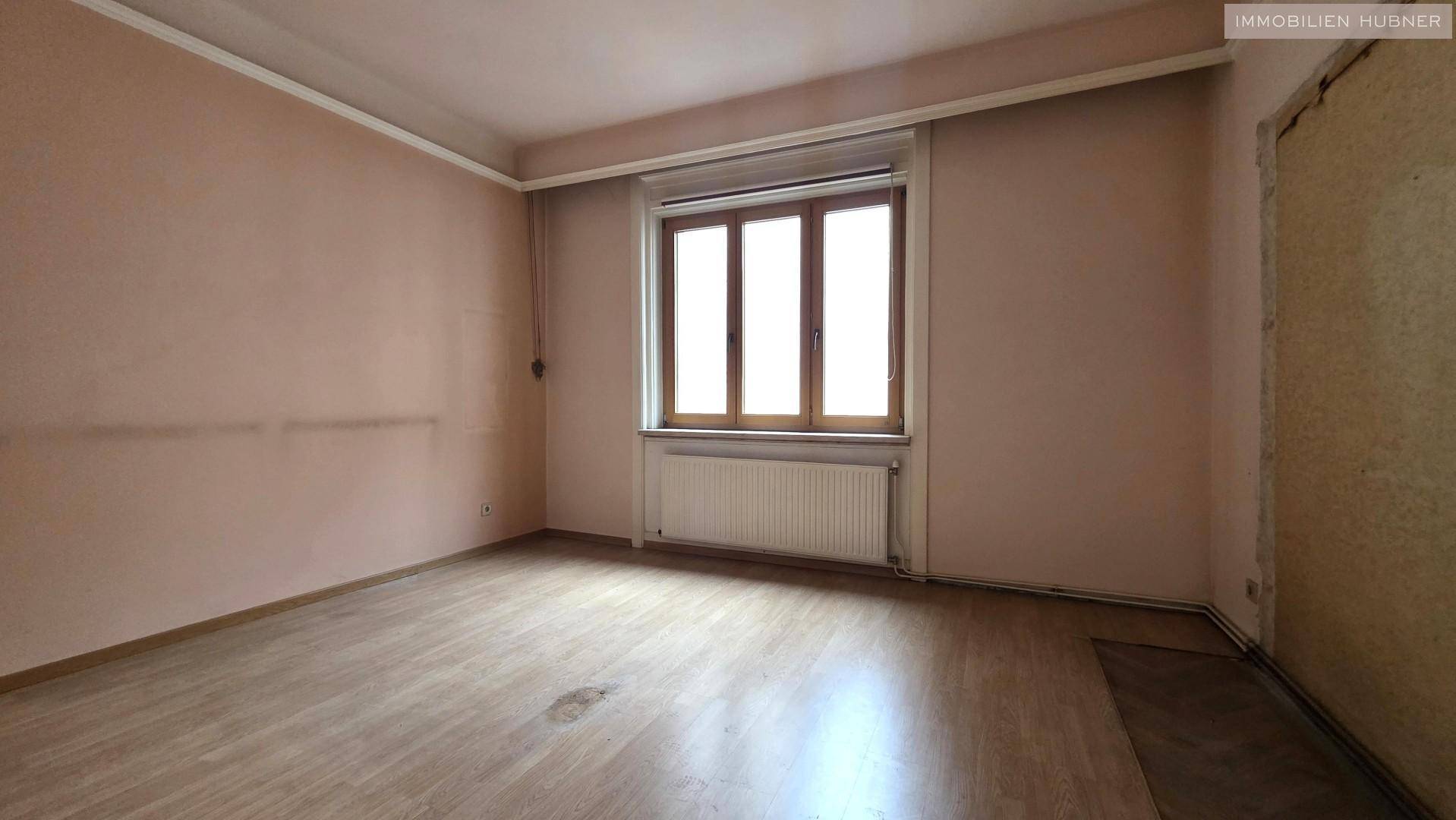 Leeres Zimmer mit rosa Wänden, Laminatboden und großem Fenster, wartet auf Renovierung.