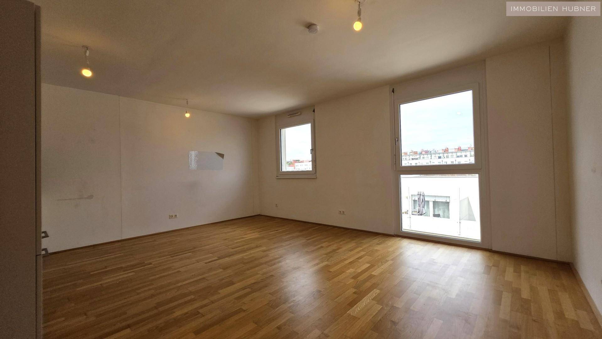 Helles, leeres Wohnzimmer mit Parkettboden und großen Fenstern, bereit zur individuellen Gestaltung.