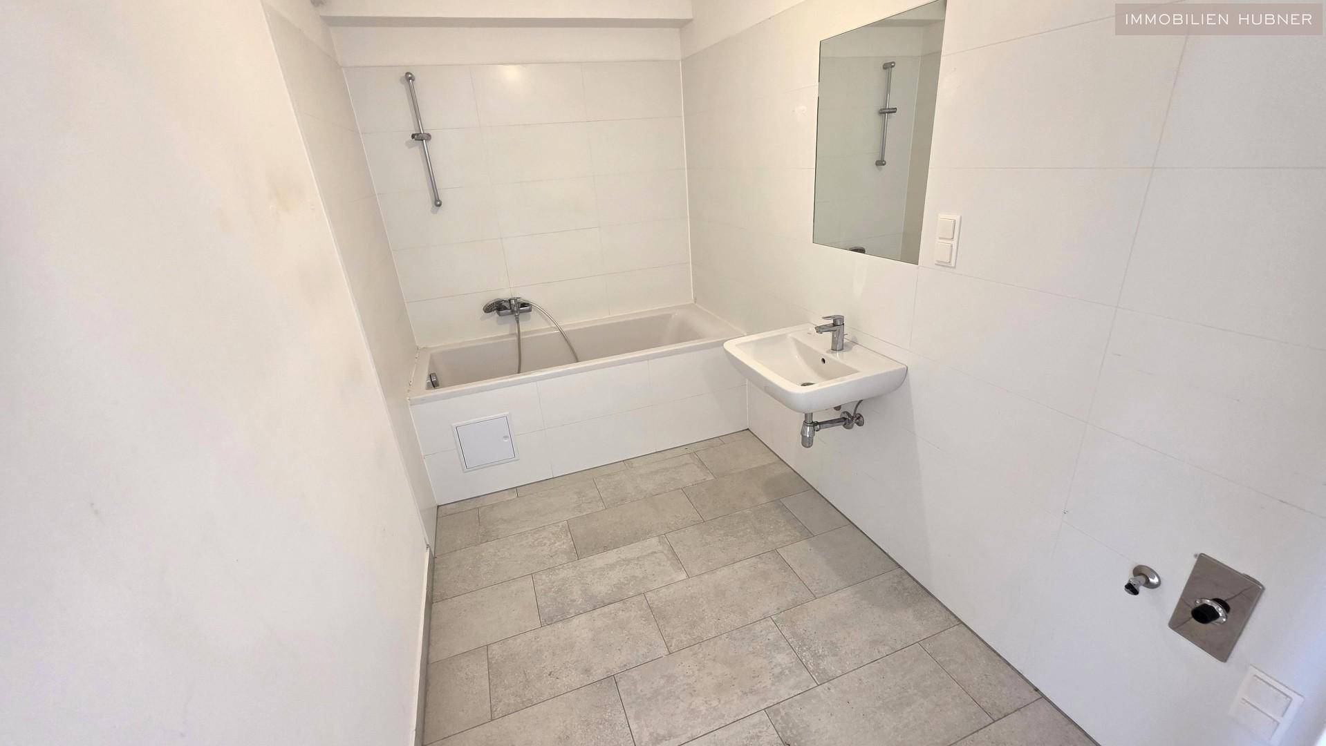 Badezimmer mit Badewanne, Waschbecken und hellen Fliesen an Wänden und Boden.