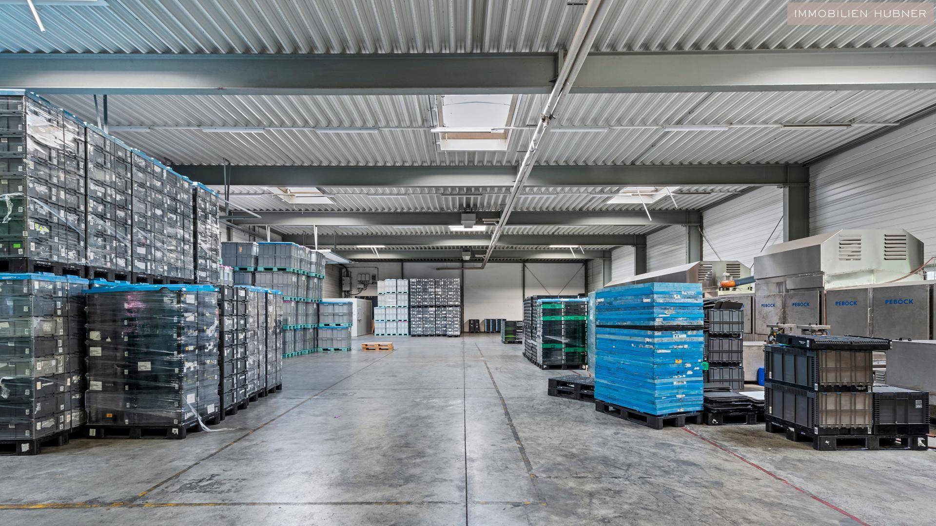 Industrielle Lagerhalle mit hohen Decken, Oberlichtern und Reihen von gestapelten Kisten und Geräten.