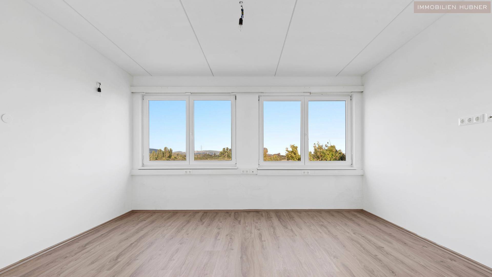 Leerer Raum mit weißen Wänden, Laminatboden und großen Fenstern mit weitem Ausblick.