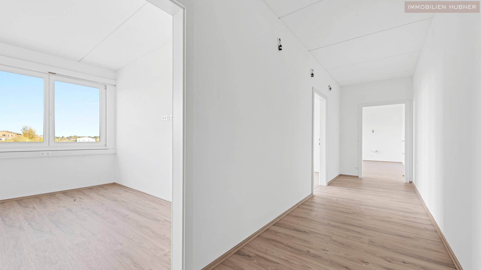 Heller Flur mit weißen Wänden, Laminatboden und Blick durch das Fenster ins Grüne.