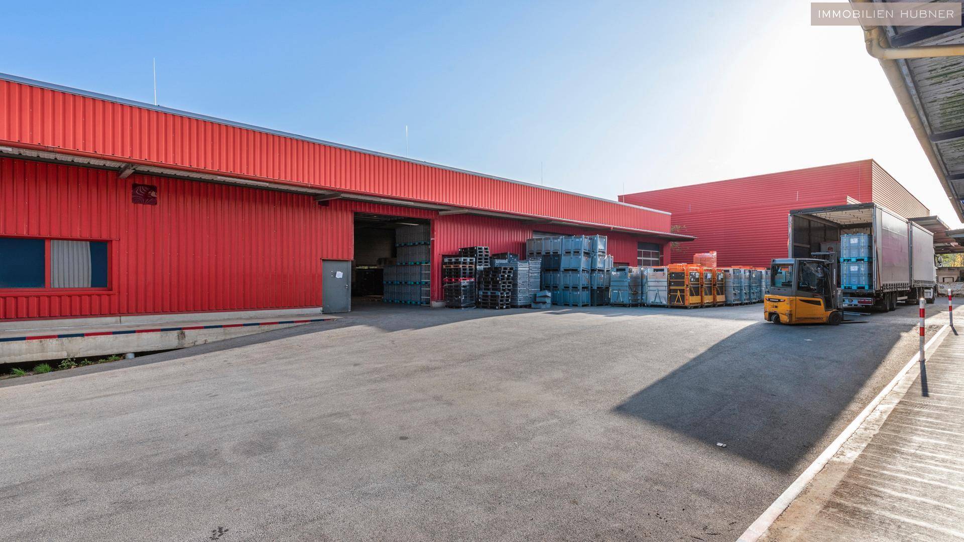Rotes Industriegebäude mit Laderampen, LKWs und Gabelstaplern auf dem Betriebsgelände.