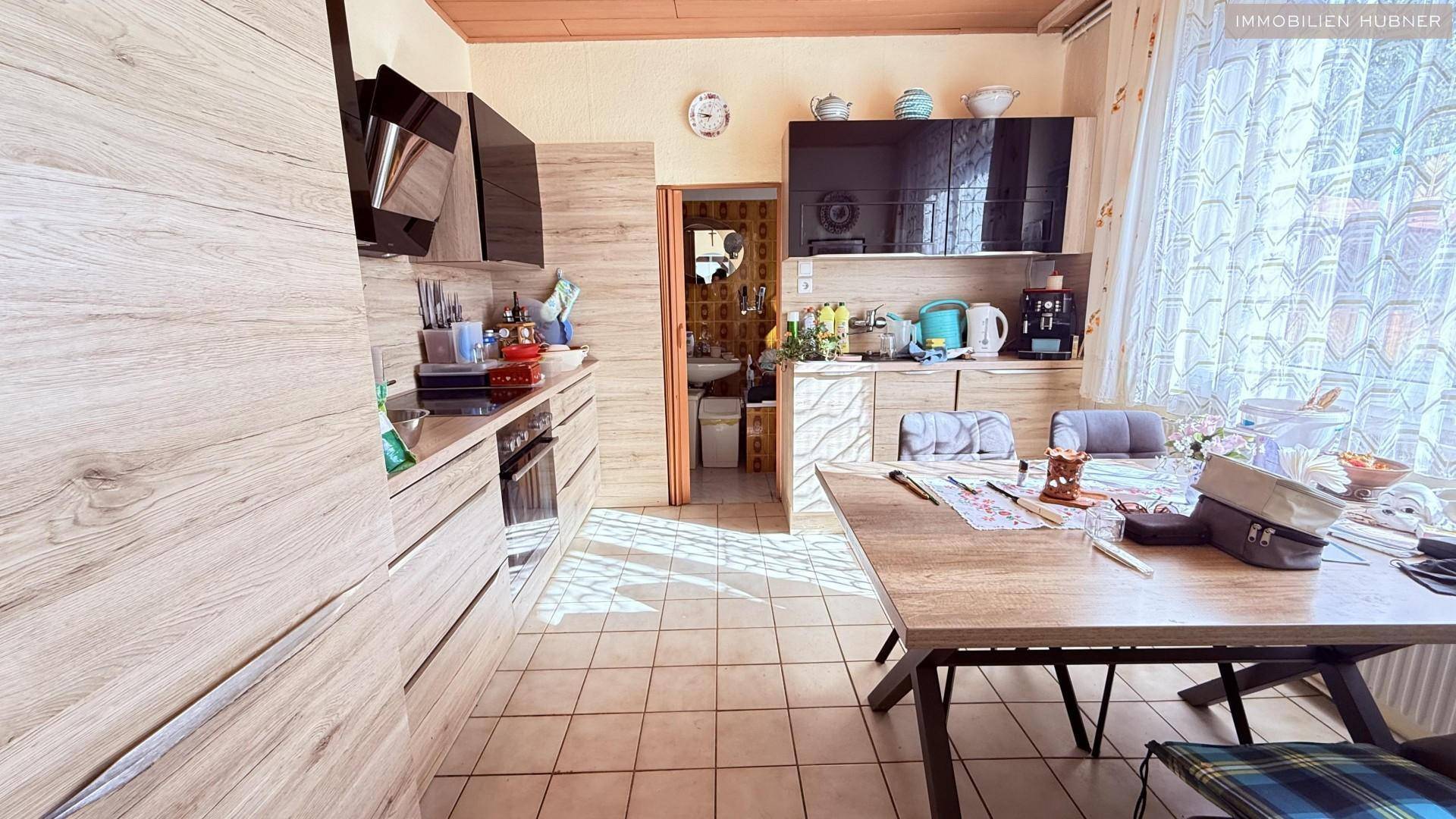 Funktionale Küche mit Holzoptik-Schränken, Fliesenboden und Essbereich am Fenster.