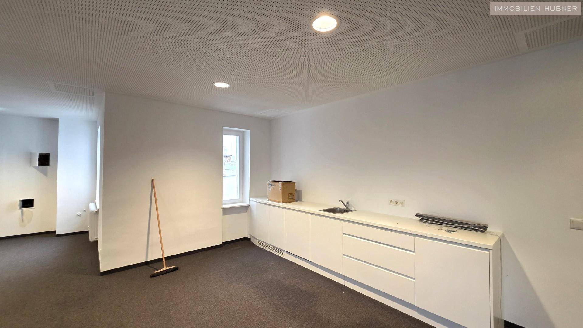 Bereich mit einer langen weißen Küchenzeile, Spülbecken und einem kleinen Fenster im Büroraum.