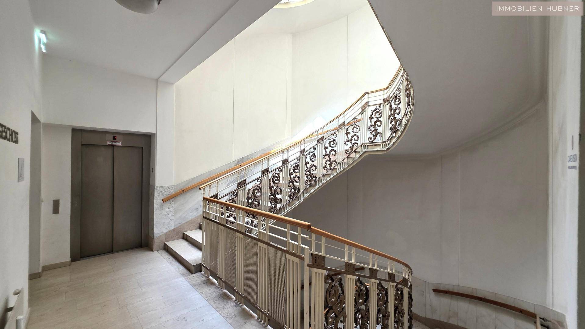 Elegantes Treppenhaus mit kunstvollem Geländer und einem modernen Aufzug, der alle Etagen erschließt.