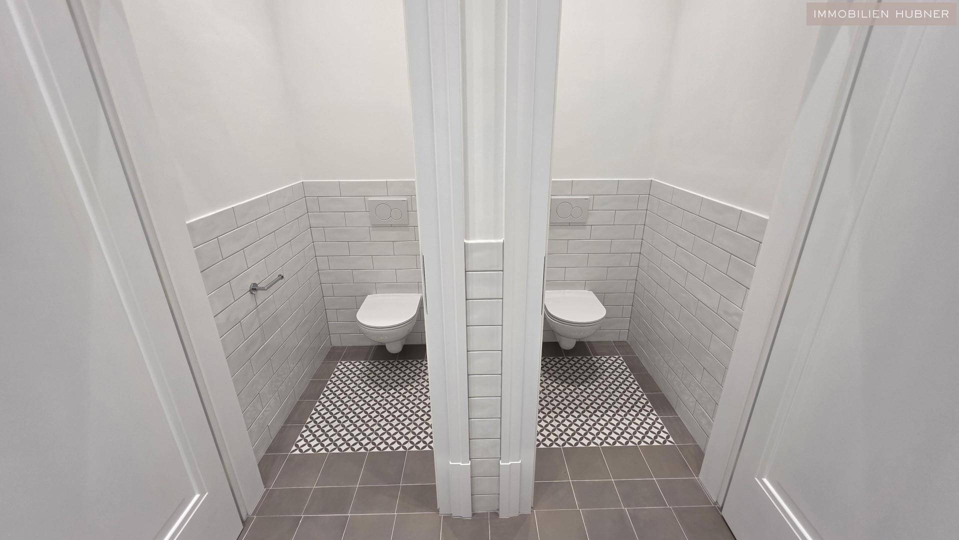 Zwei separate Toilettenkabinen mit modernen Wand-WCs und stilvollen Fliesen im Bodenbereich.