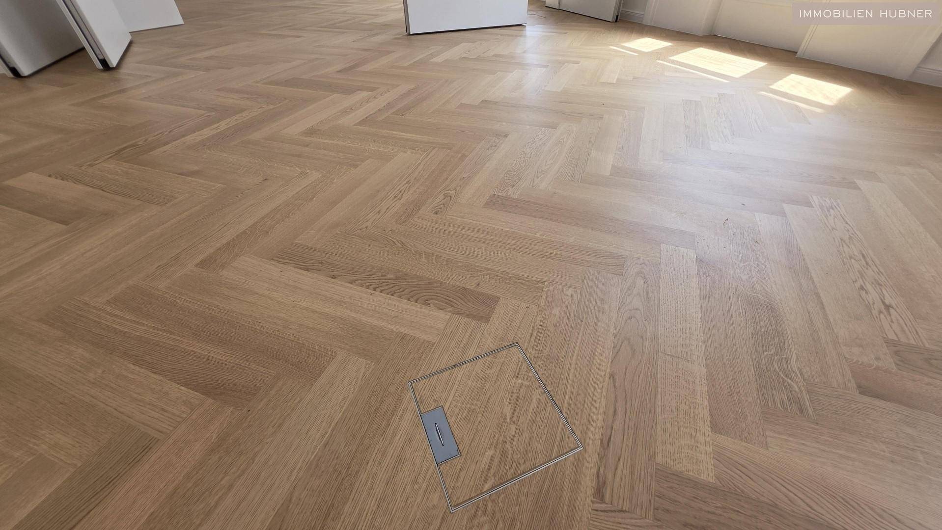 Nahaufnahme des hochwertigen Fischgrätparketts mit einer Bodensteckdose, die Funktionalität bietet.