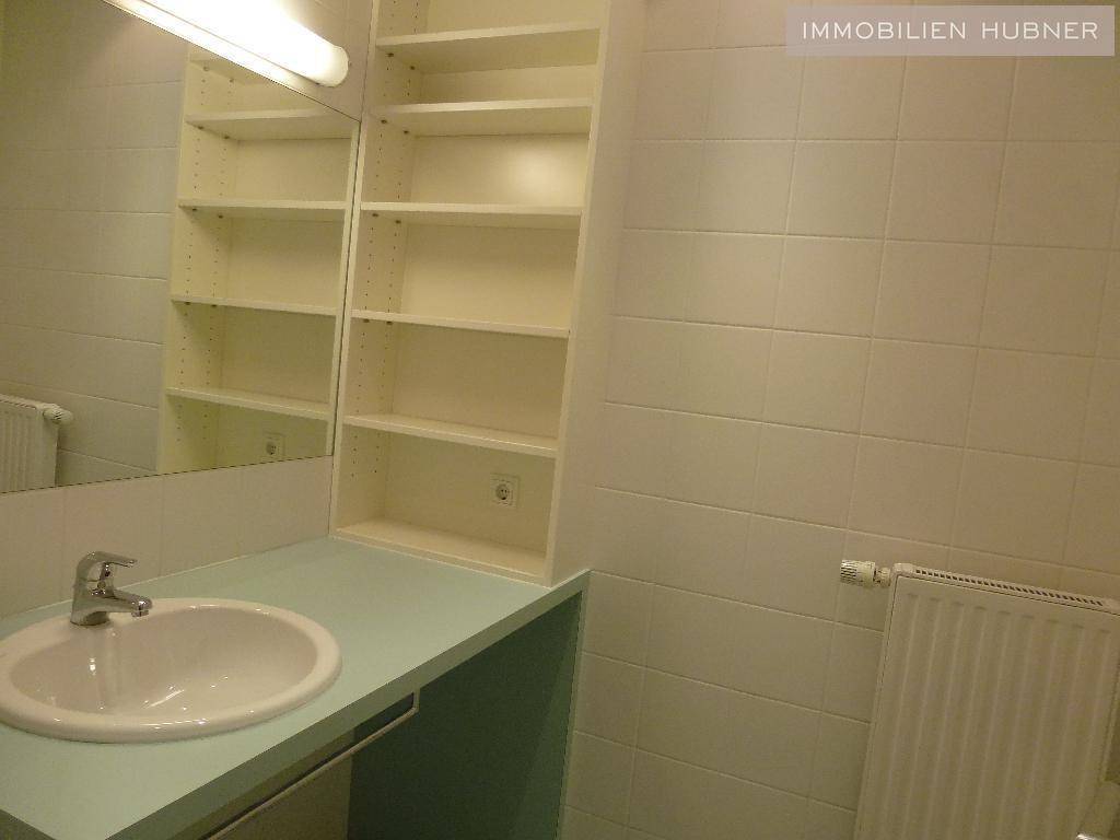 Badezimmer mit Waschbecken, großem Spiegel und praktischen Einbauregalen für zusätzlichen Stauraum.