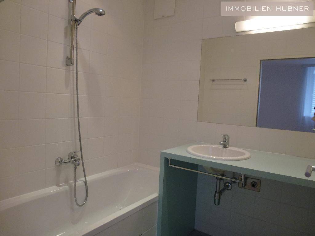 Badezimmer mit weiß gefliesten Wänden, Badewanne mit Duschfunktion und einem Waschbecken mit hellblauer Ablage.