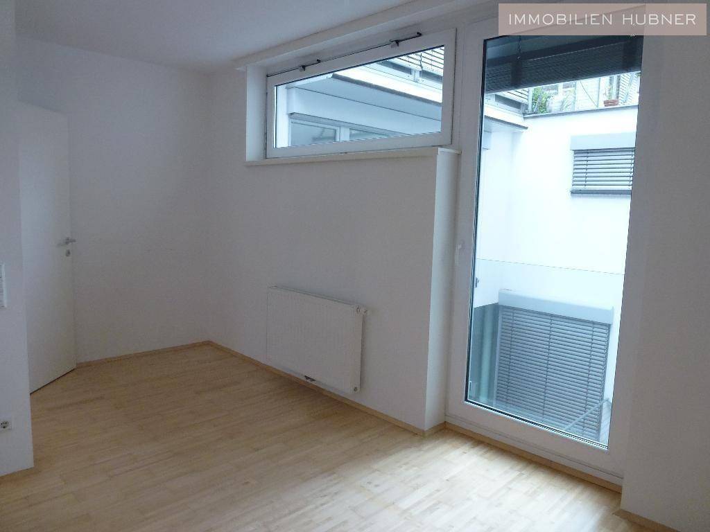 Leeres Zimmer mit hellem Parkettboden und Fensterfront zum ruhigen Innenhof mit Jalousien.