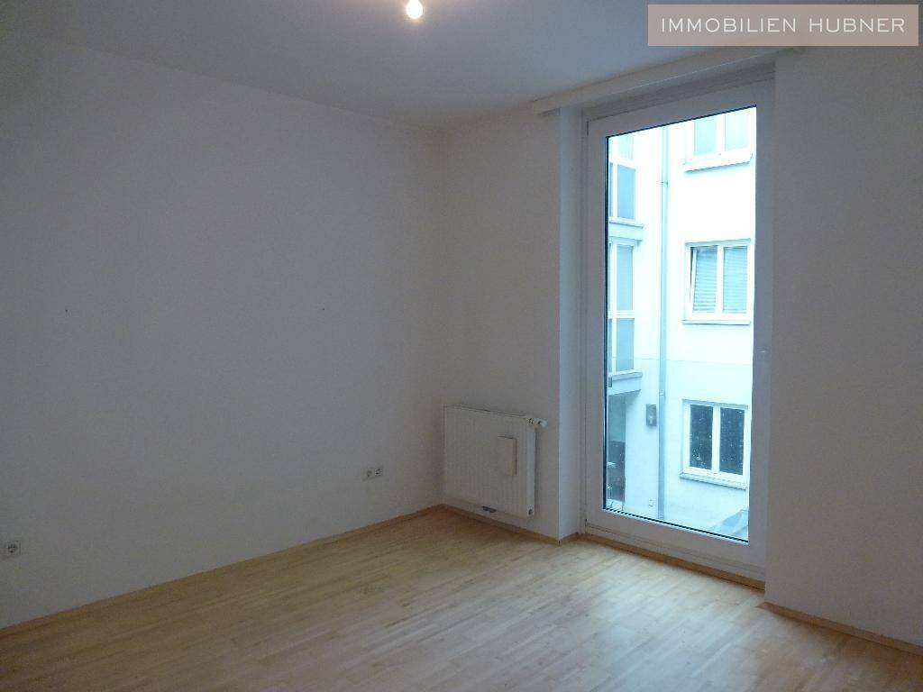 Helles Zimmer mit Parkettboden und bodentiefem Fenster, das einen Blick auf den Innenhof bietet.