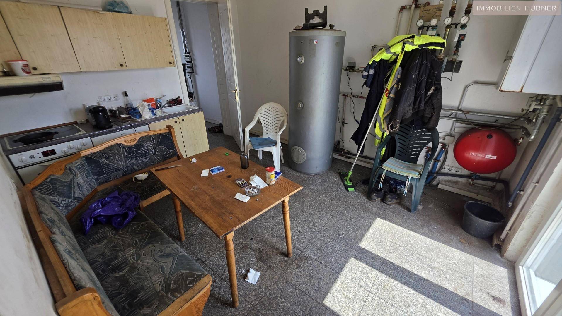 Einfache Küche mit Essbereich und angrenzendem Technikraum mit Warmwasserspeicher.