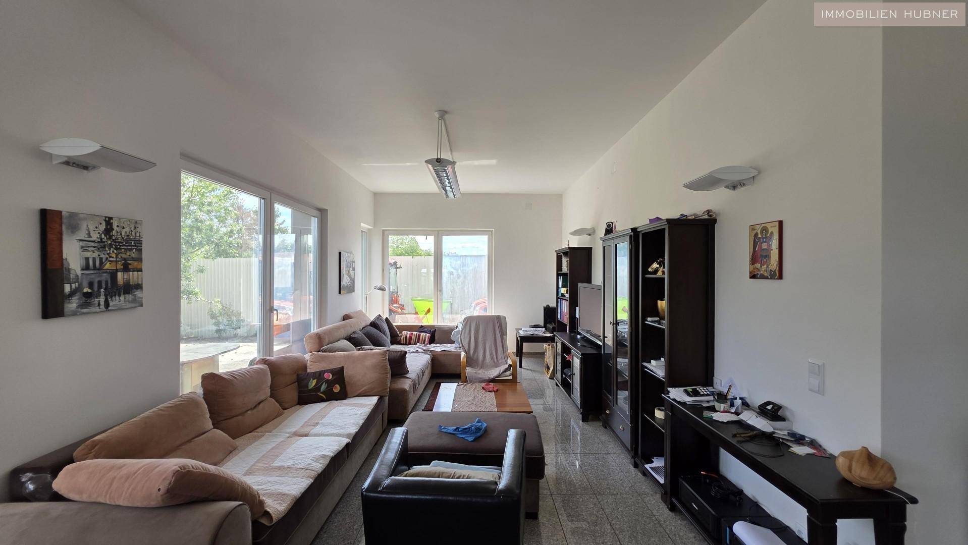 Geräumiges Wohnzimmer mit beigen Sofas, dunklen Möbeln und großen Fenstern zum Garten.