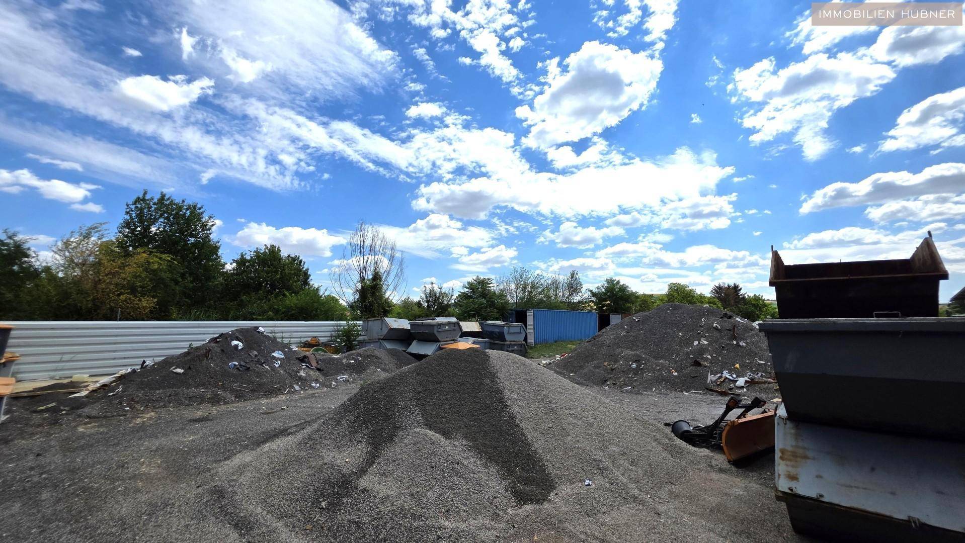 Große Schotterhaufen und Container auf einem Außengelände unter bewölktem Himmel.