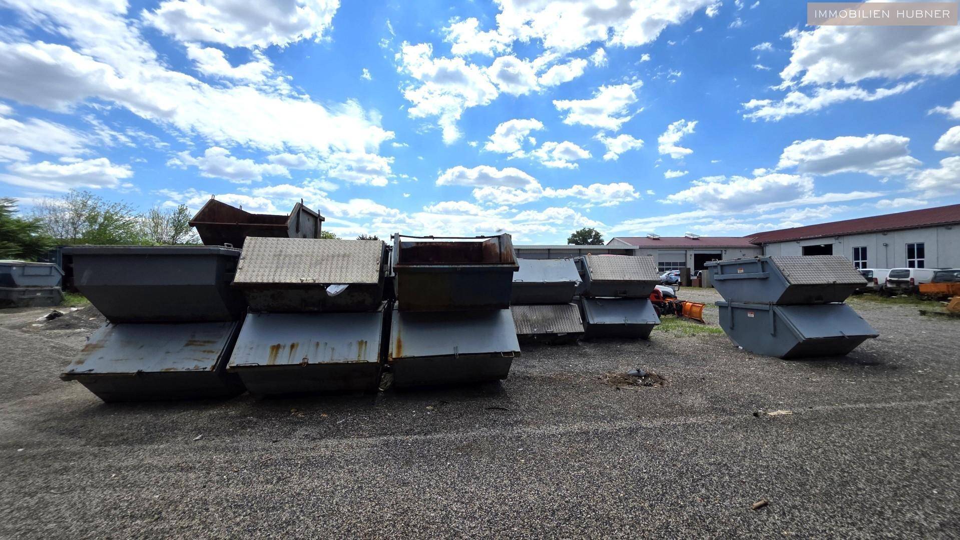 Mehrere große Abfallcontainer auf einem Schotterplatz vor einem Gebäude.