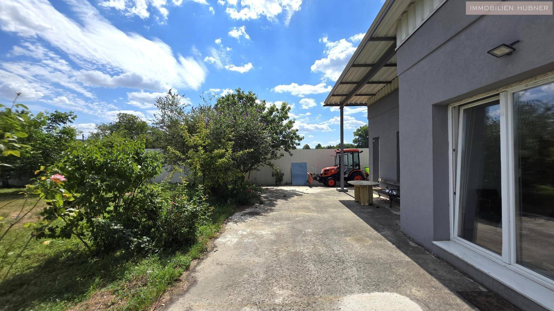 Kleiner Gartenbereich neben dem Gebäude mit Betonweg und grünen Pflanzen unter blauem Himmel.