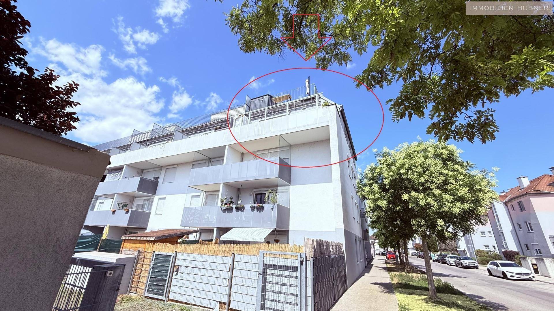 Gesamtansicht des modernen Mehrfamilienhauses von der Straße aus, umgeben von Bäumen und einer städtischen Umgebung.