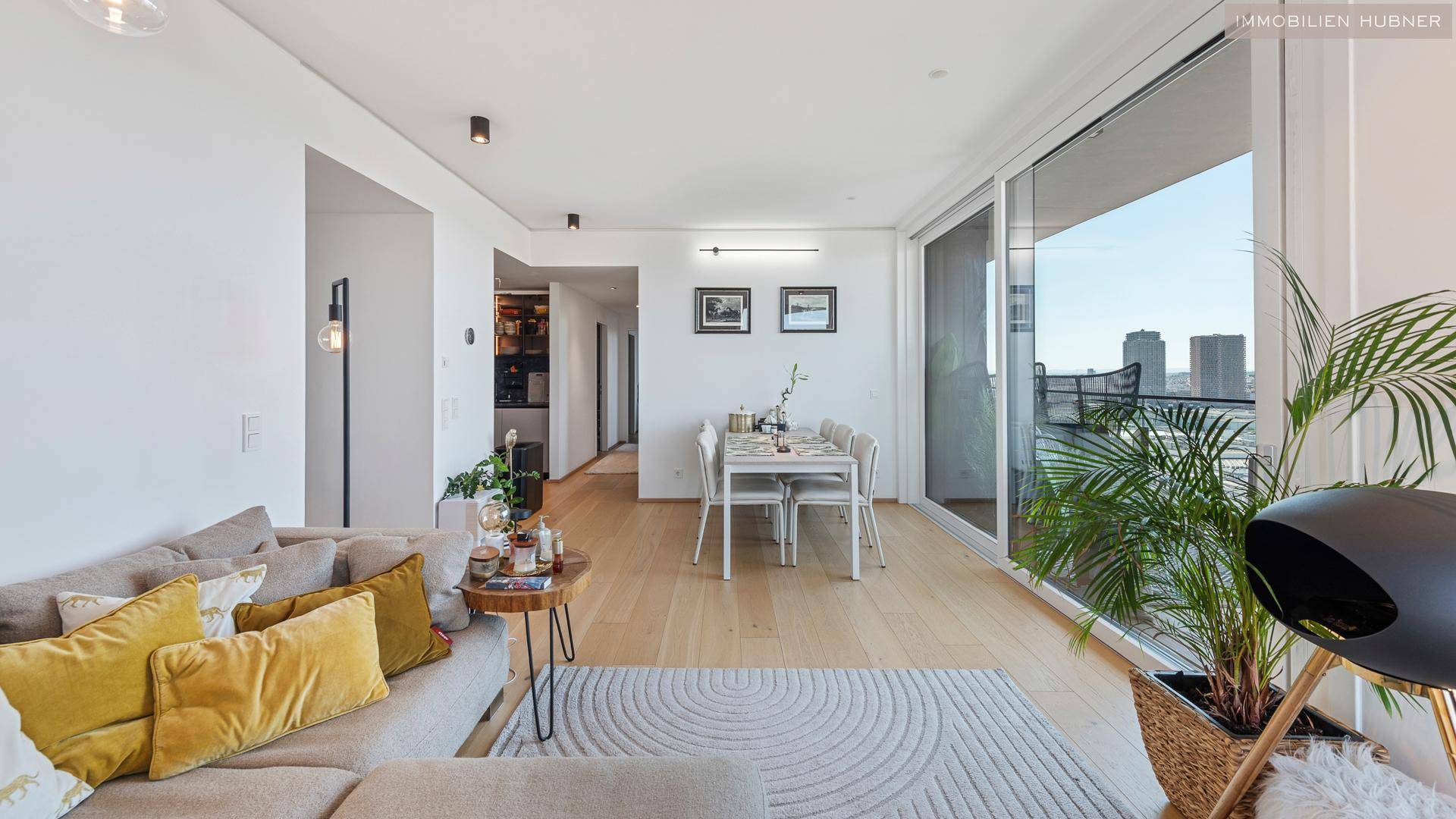 Geräumiger Wohn- und Essbereich mit beigem Sofa, Holzboden und Zugang zu einem Balkon mit Stadtblick.