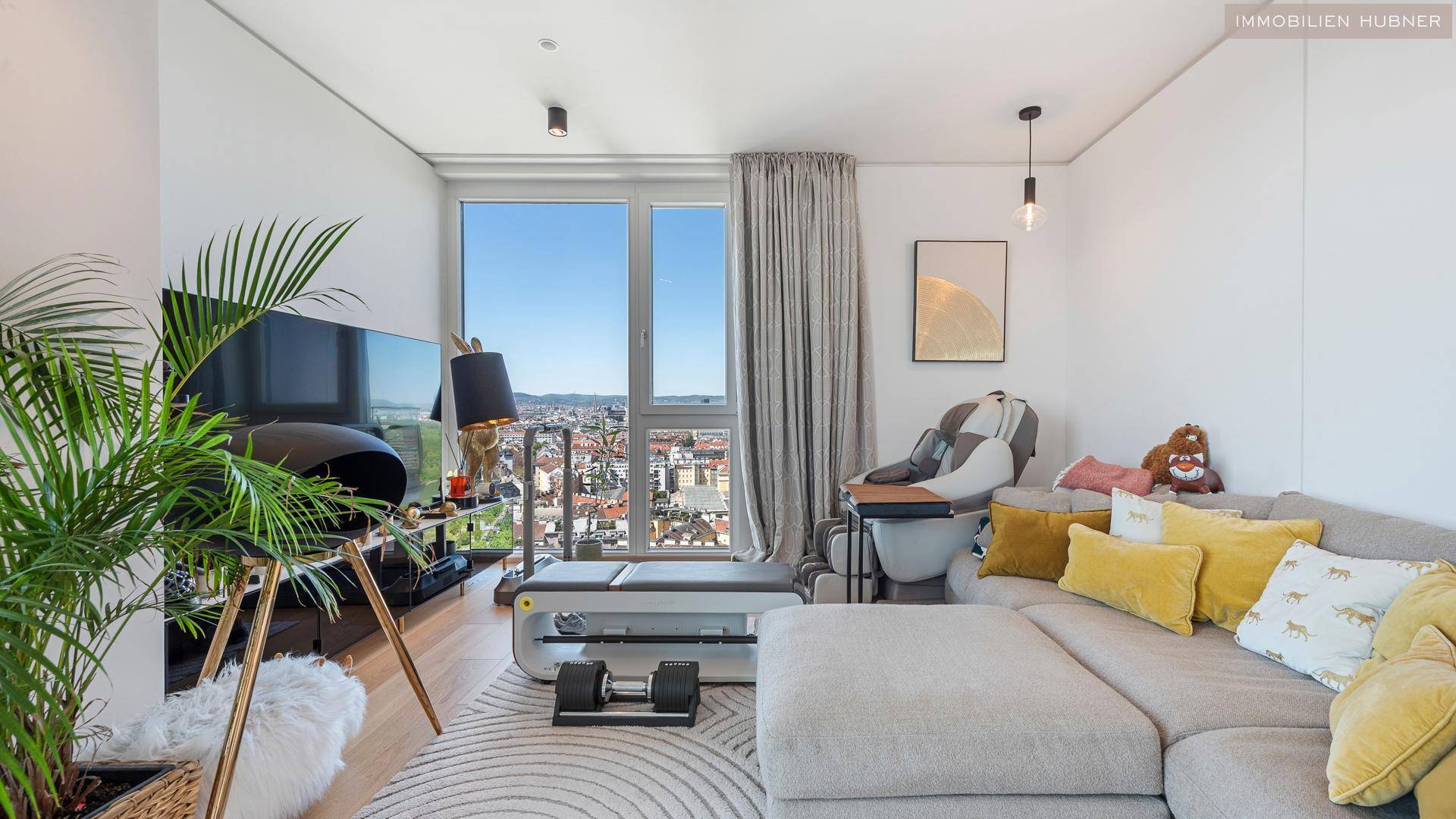 Gemütliches Wohnzimmer mit Sofa, Fernseher und großem Fenster mit Blick auf die Stadt.