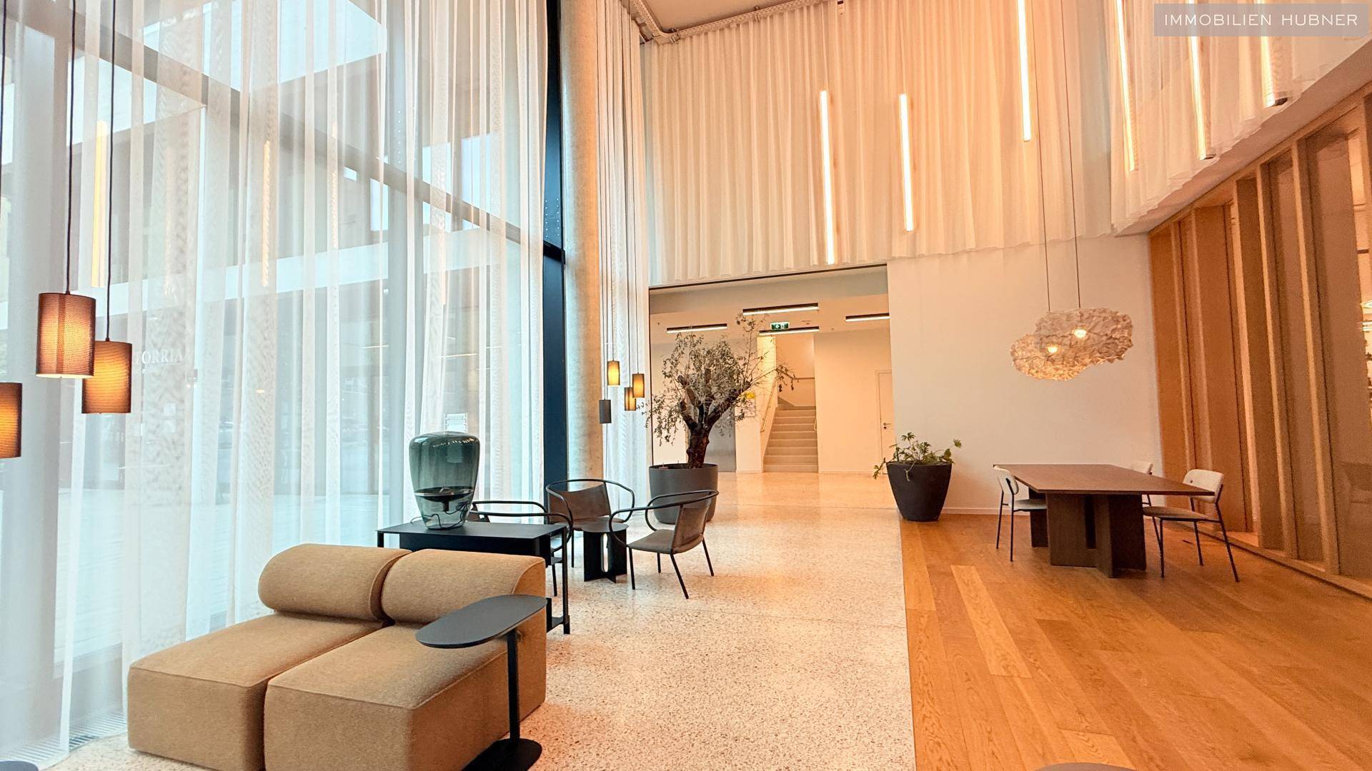 Stilvolle Lobby mit hohen Decken, großen Fenstern und bequemen Sitzbereichen.