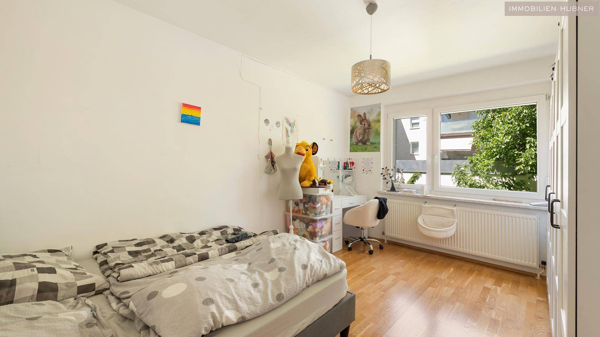 Helles Kinderzimmer mit Holzboden, Schreibtisch und Fenster mit Blick ins Grüne.