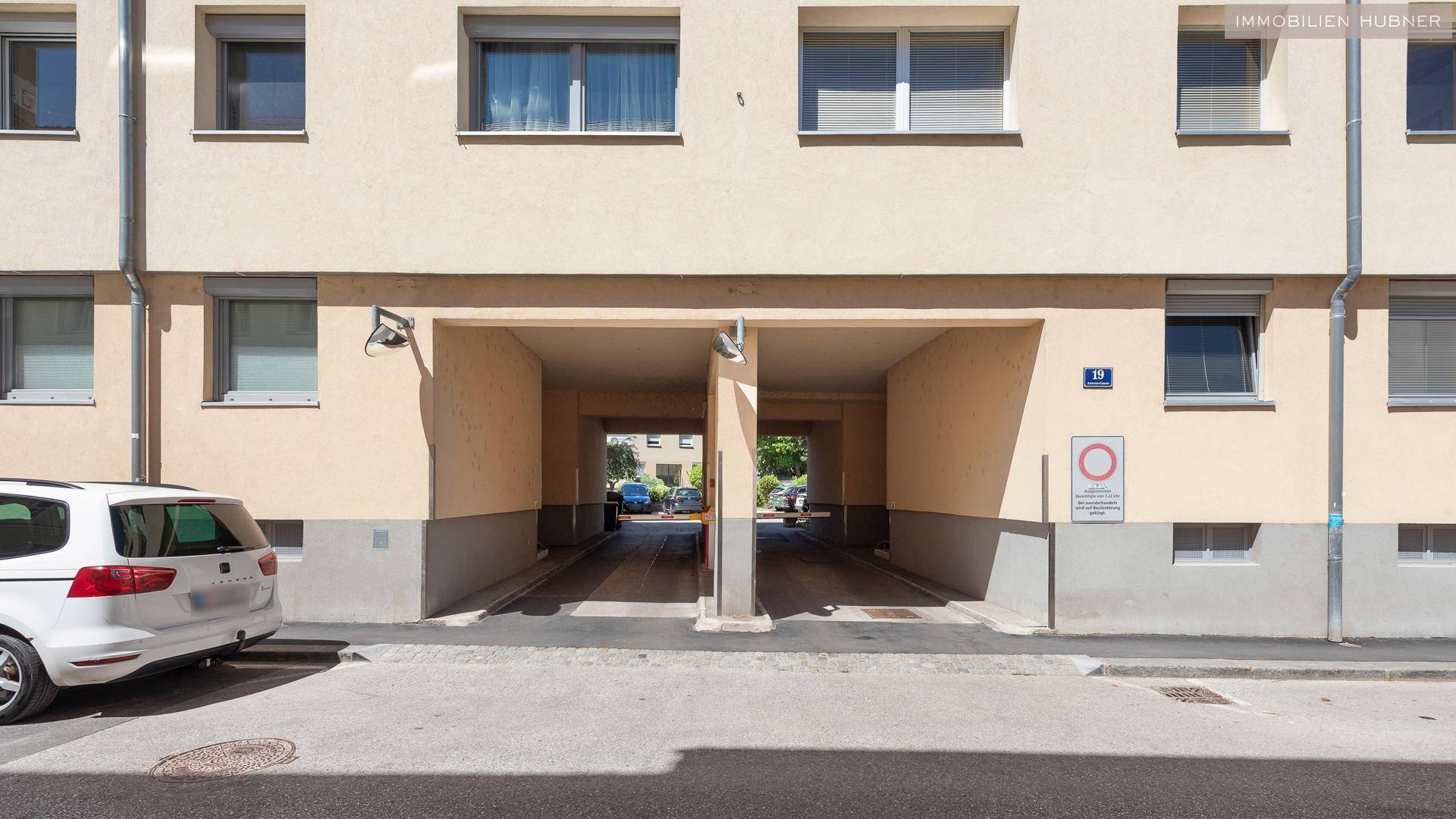 Gebäudefassade mit zwei überdachten Durchfahrten, die zu Parkmöglichkeiten führen.