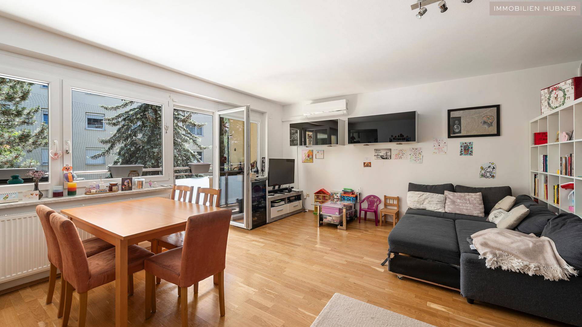 Heller Wohn-Essbereich mit Holzboden, großzügigen Fenstern und Zugang zum Balkon.