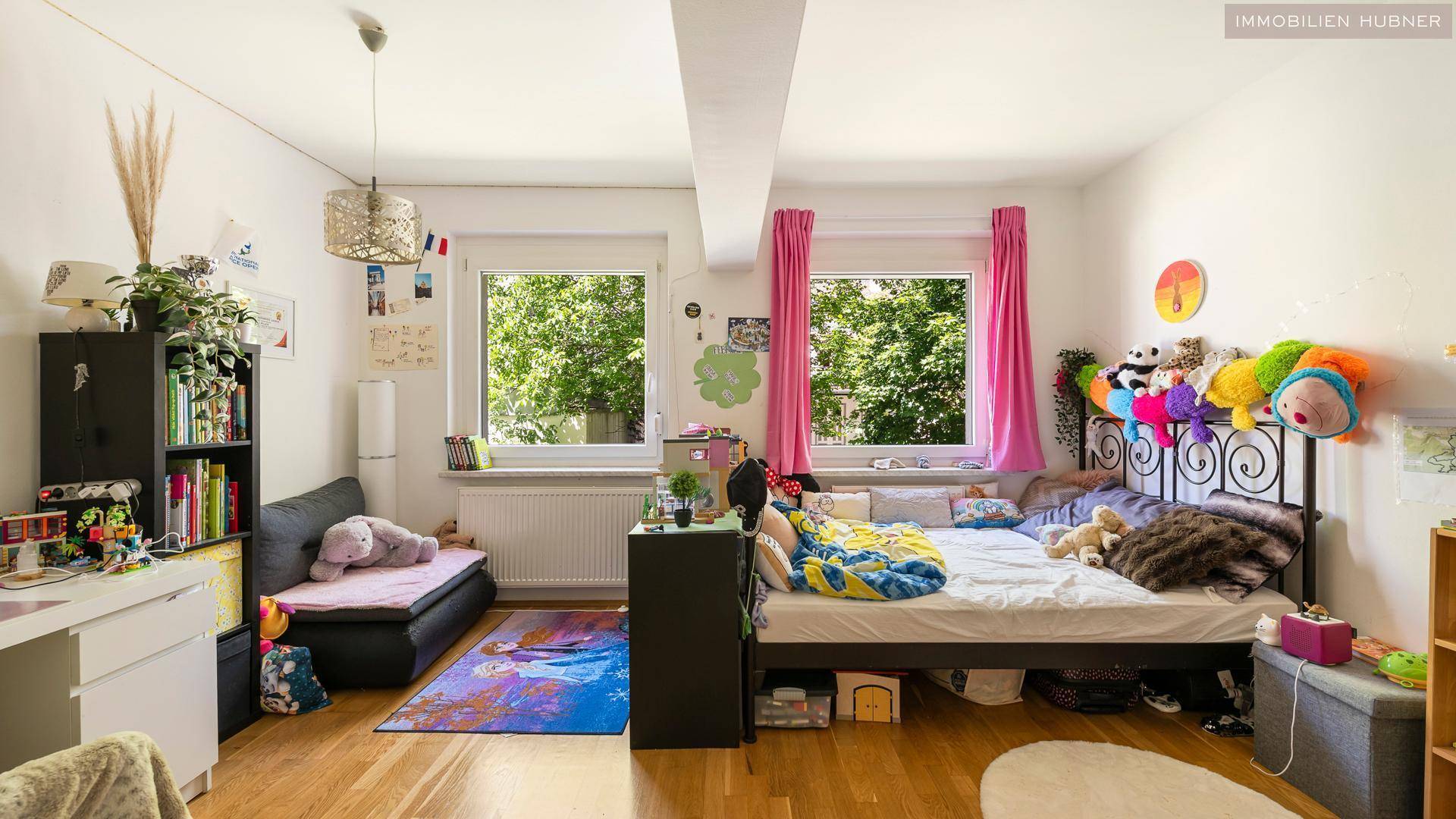 Farbenfrohes Kinderzimmer mit Holzboden, zwei Fenstern und viel Tageslicht.