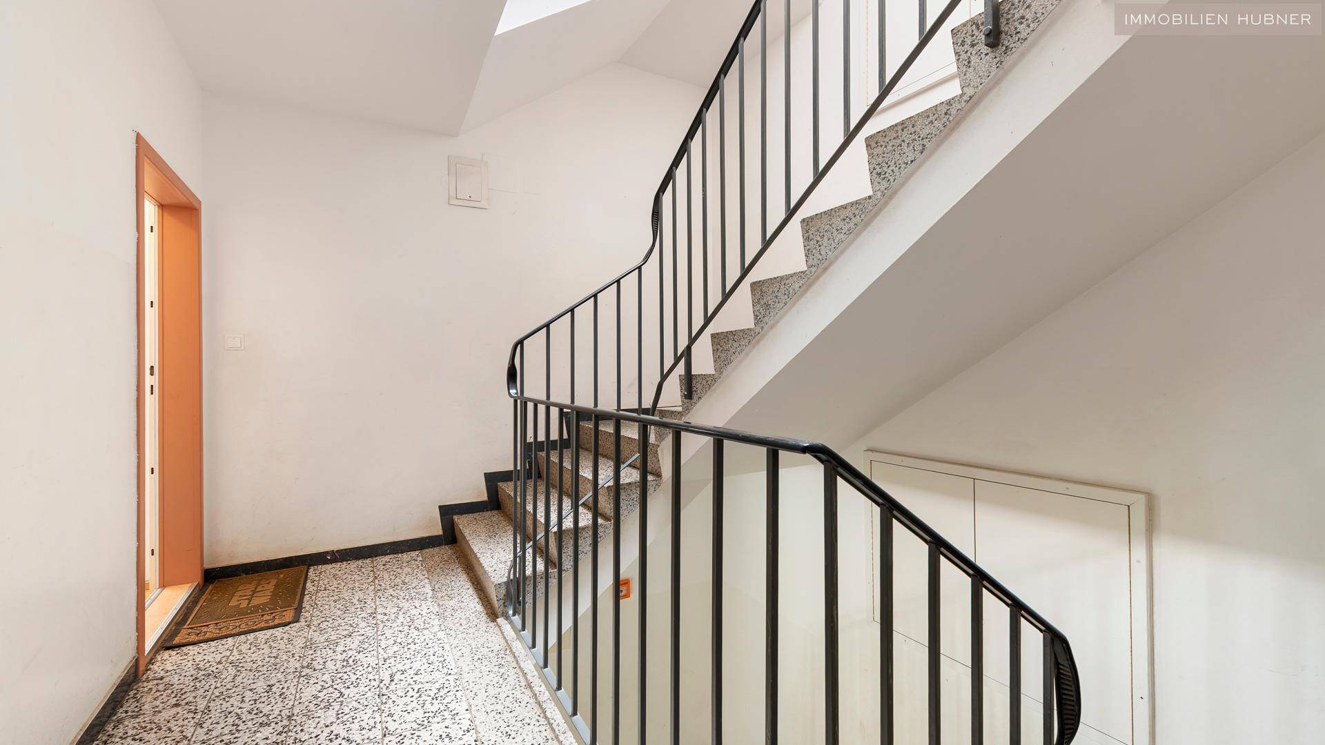 Treppenhaus mit Terrazzoboden und schmiedeeisernem Geländer, das die Etagen verbindet.