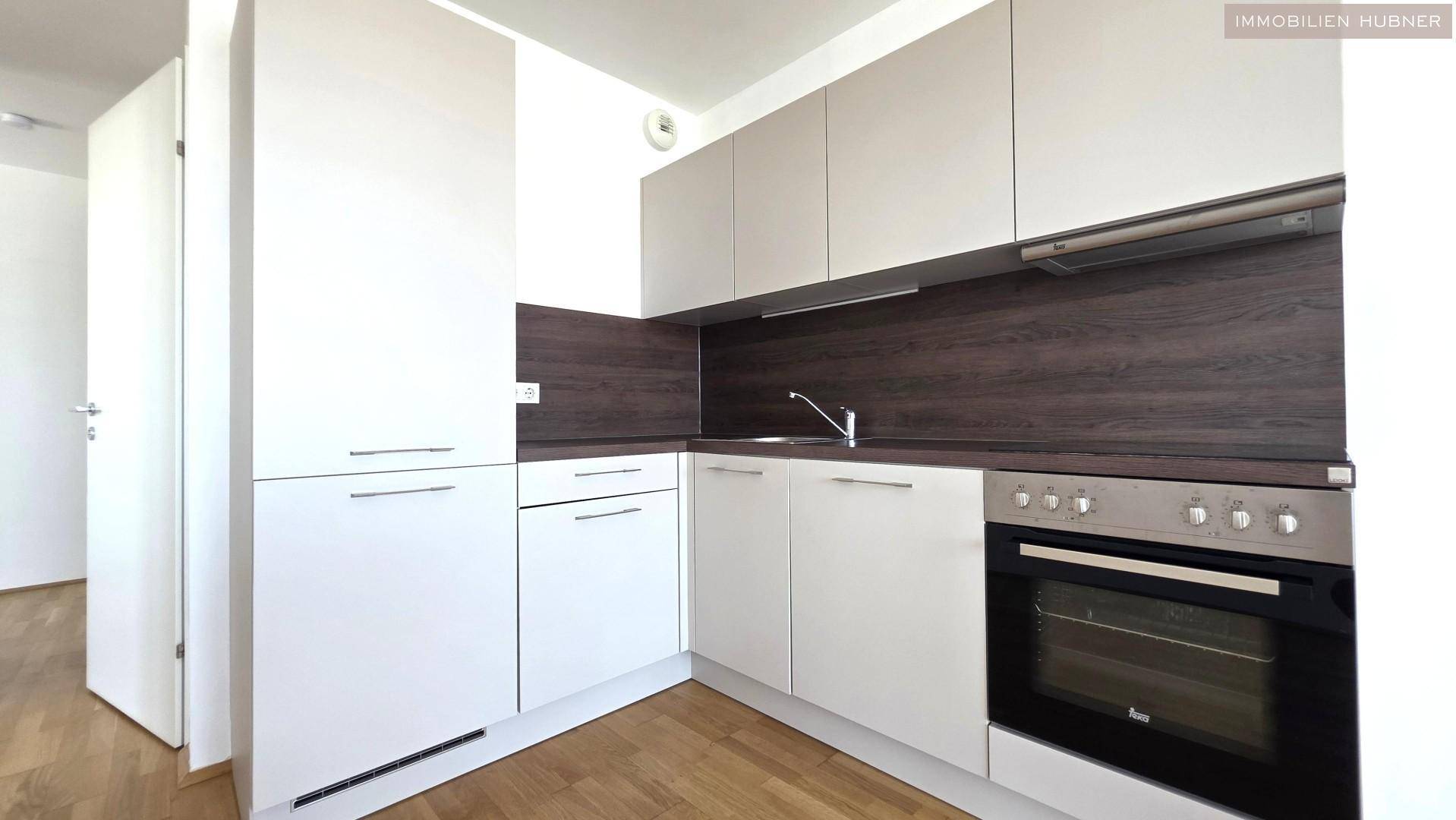 Moderne Einbauküche mit weißen und grauen Schränken, ausgestattet mit Backofen und Spüle.