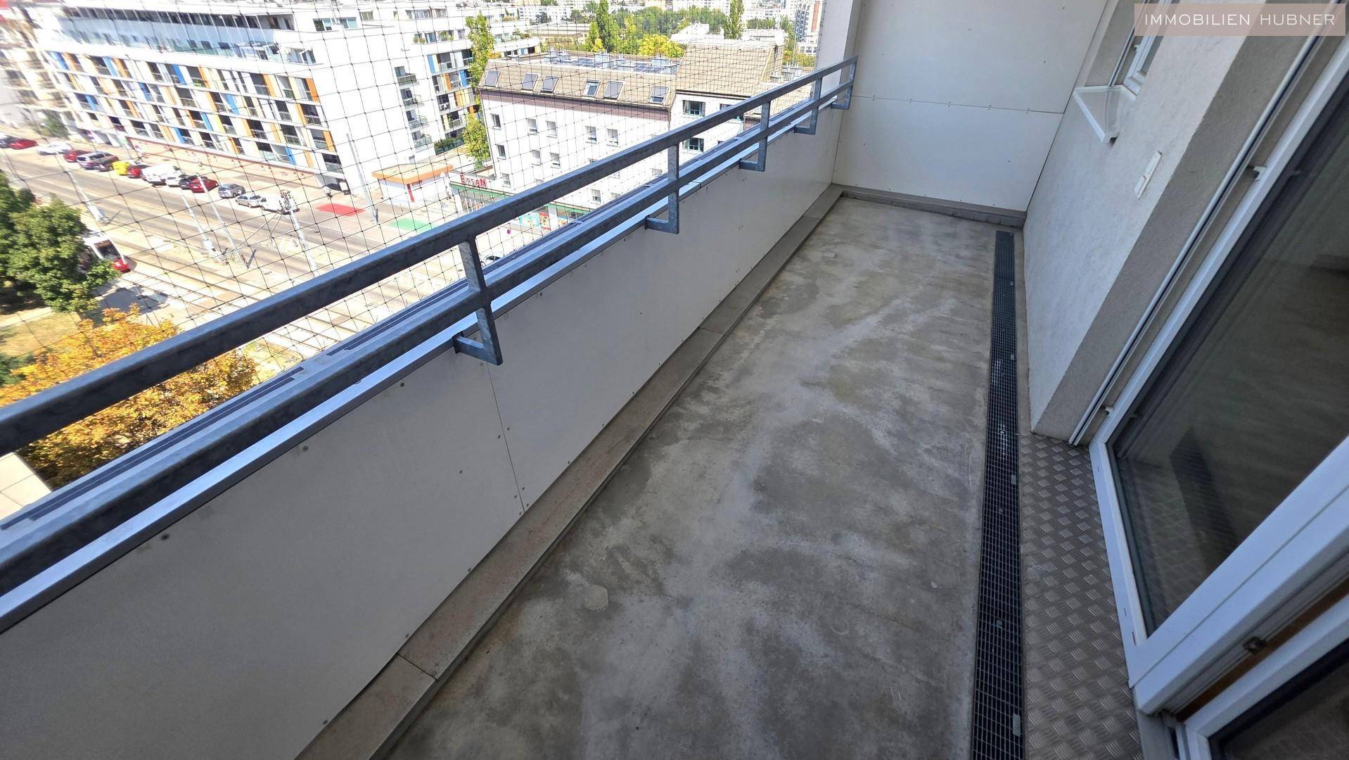 Langer Balkon mit Betonboden und Metallgeländer, bietet einen Blick auf die Stadt.