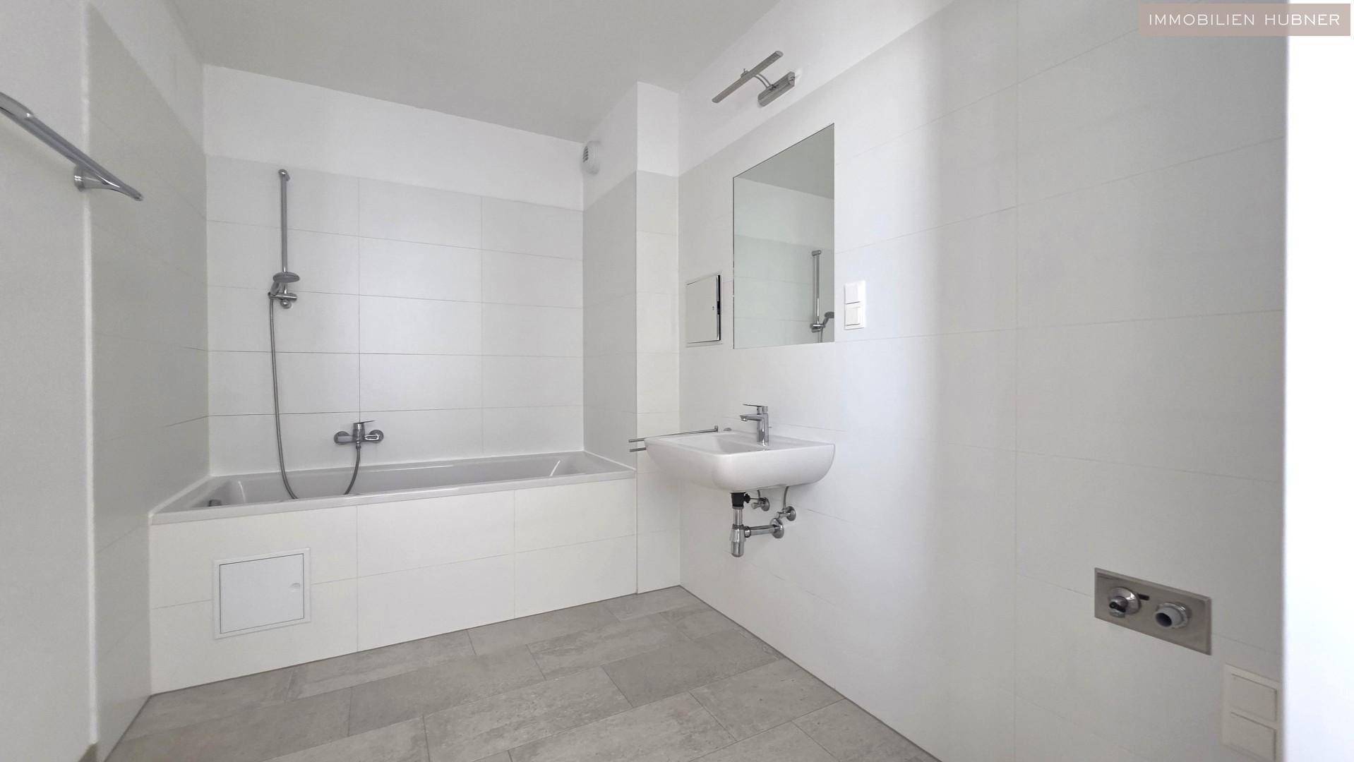 Modernes Badezimmer mit weißen Fliesen, Badewanne mit Duschfunktion und Waschbecken.