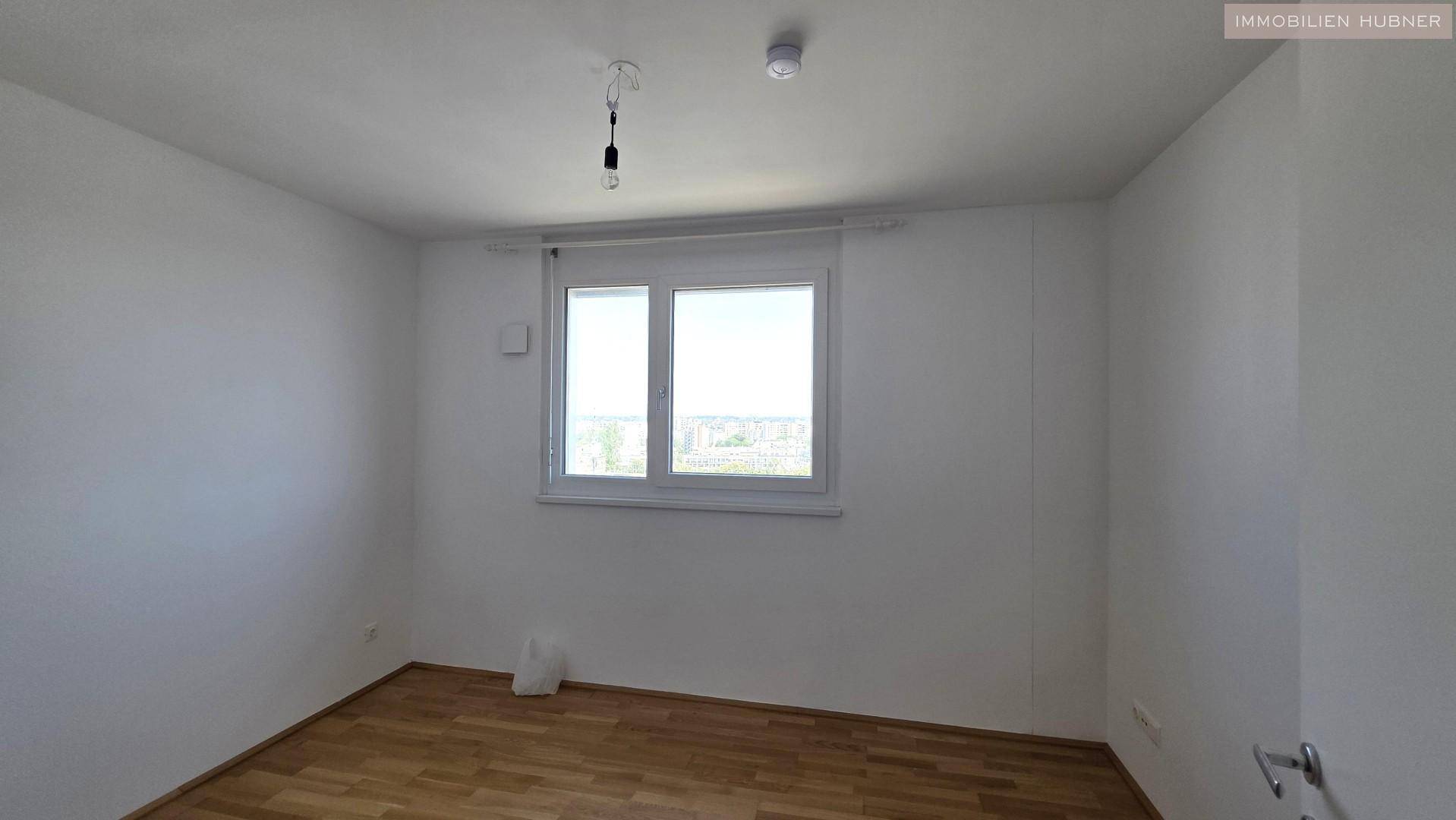 Helles Schlafzimmer mit Parkettboden und einem Fenster, das Tageslicht hereinlässt.