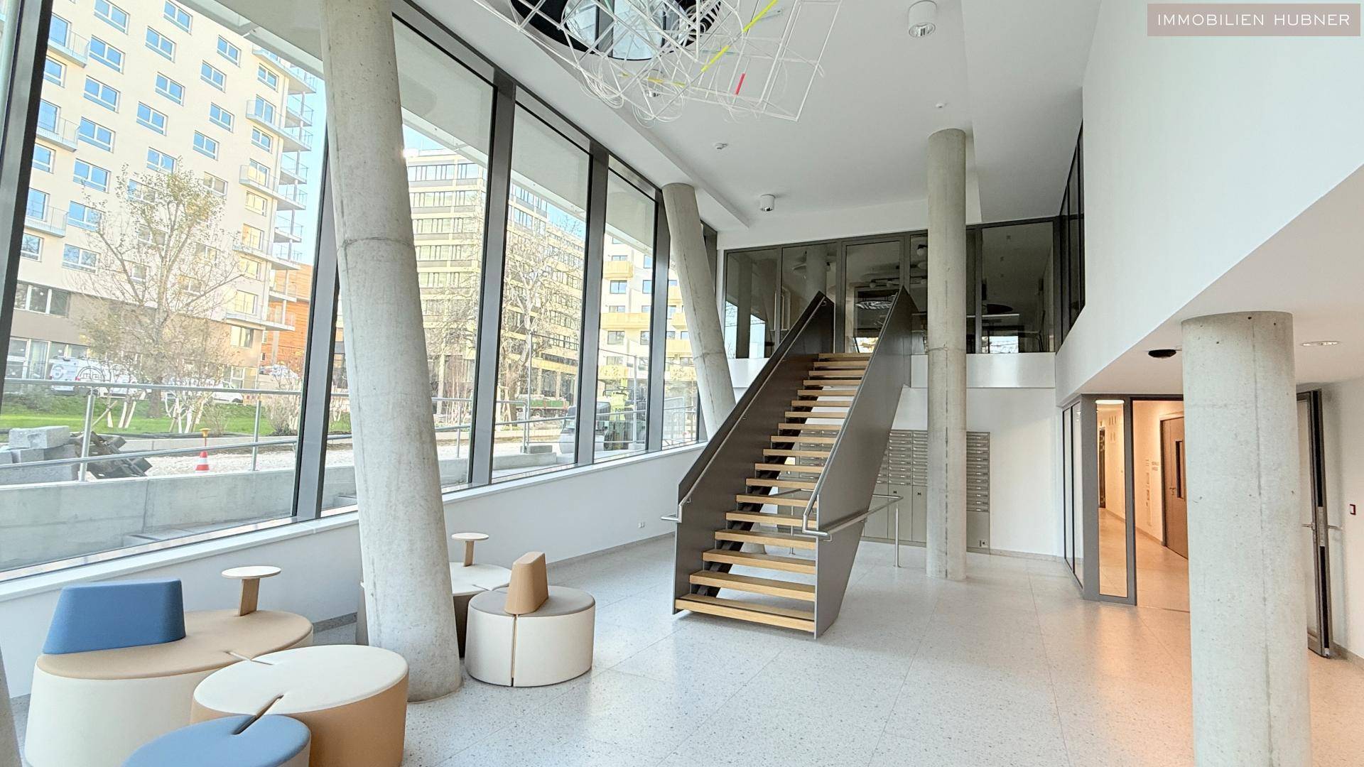 Helle, moderne Lobby mit hohen Decken, großen Fenstern und einer eleganten Treppe.