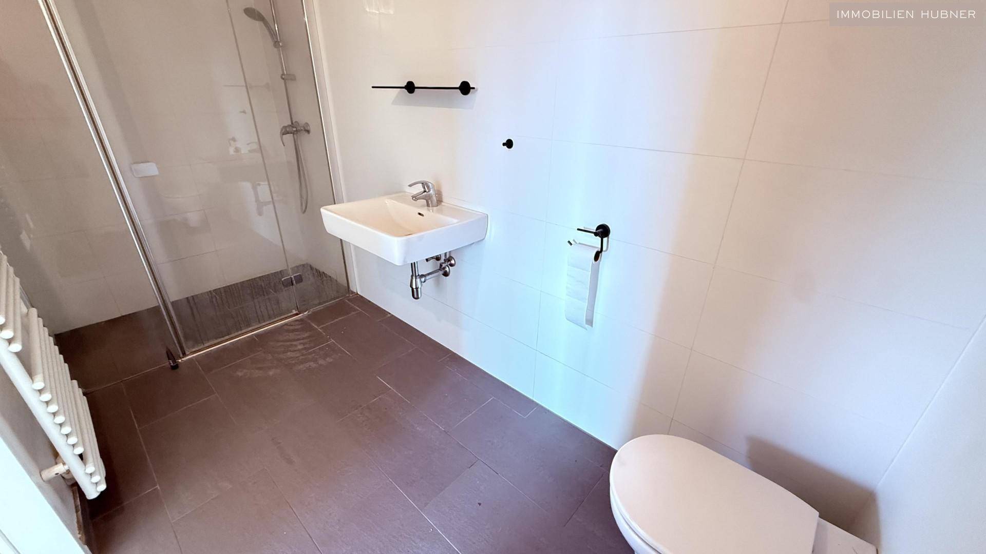 Zweites Badezimmer mit ebenerdiger Dusche, Einzelwaschbecken und WC, modern gestaltet.