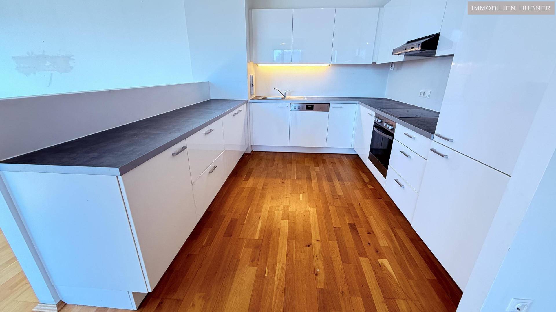 Moderne Einbauküche mit weißen Hochglanzfronten, dunklen Arbeitsplatten und integrierten Geräten.