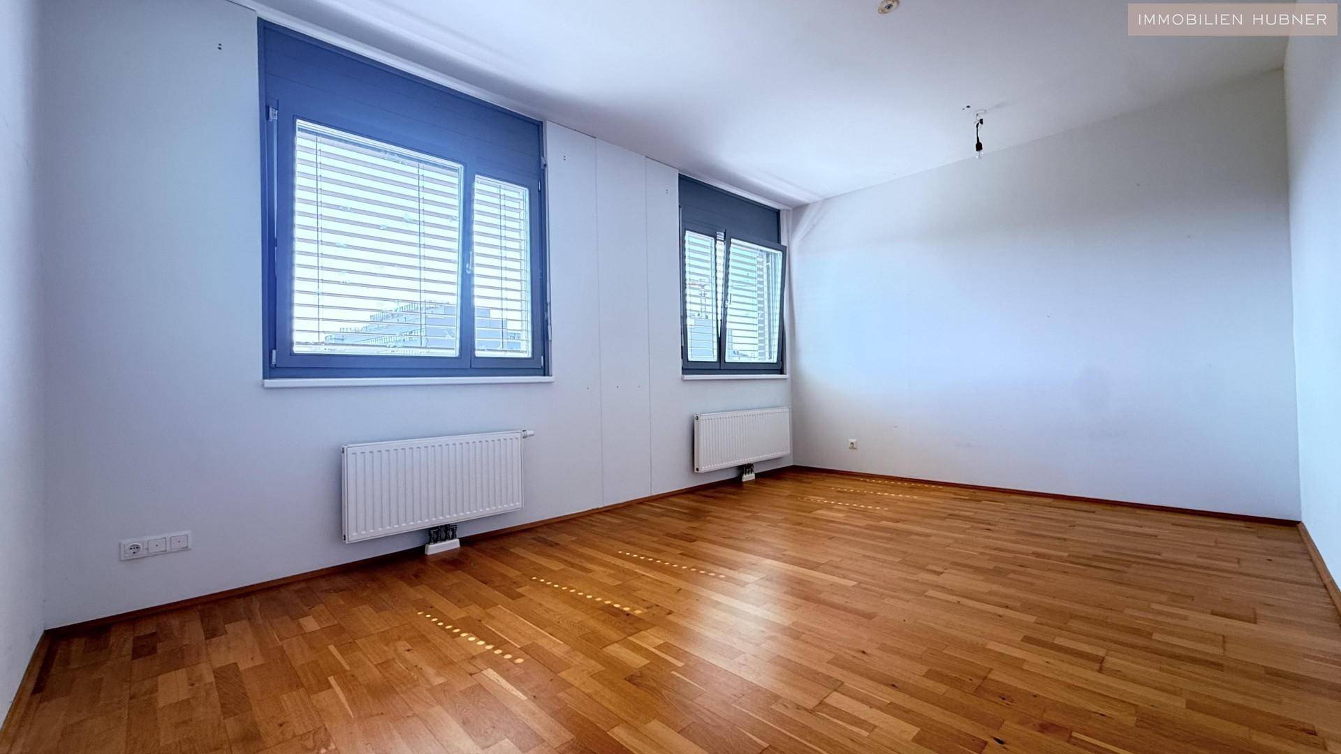 Helles Schlafzimmer mit Holzboden und zwei Fenstern, die für gute Belichtung sorgen.